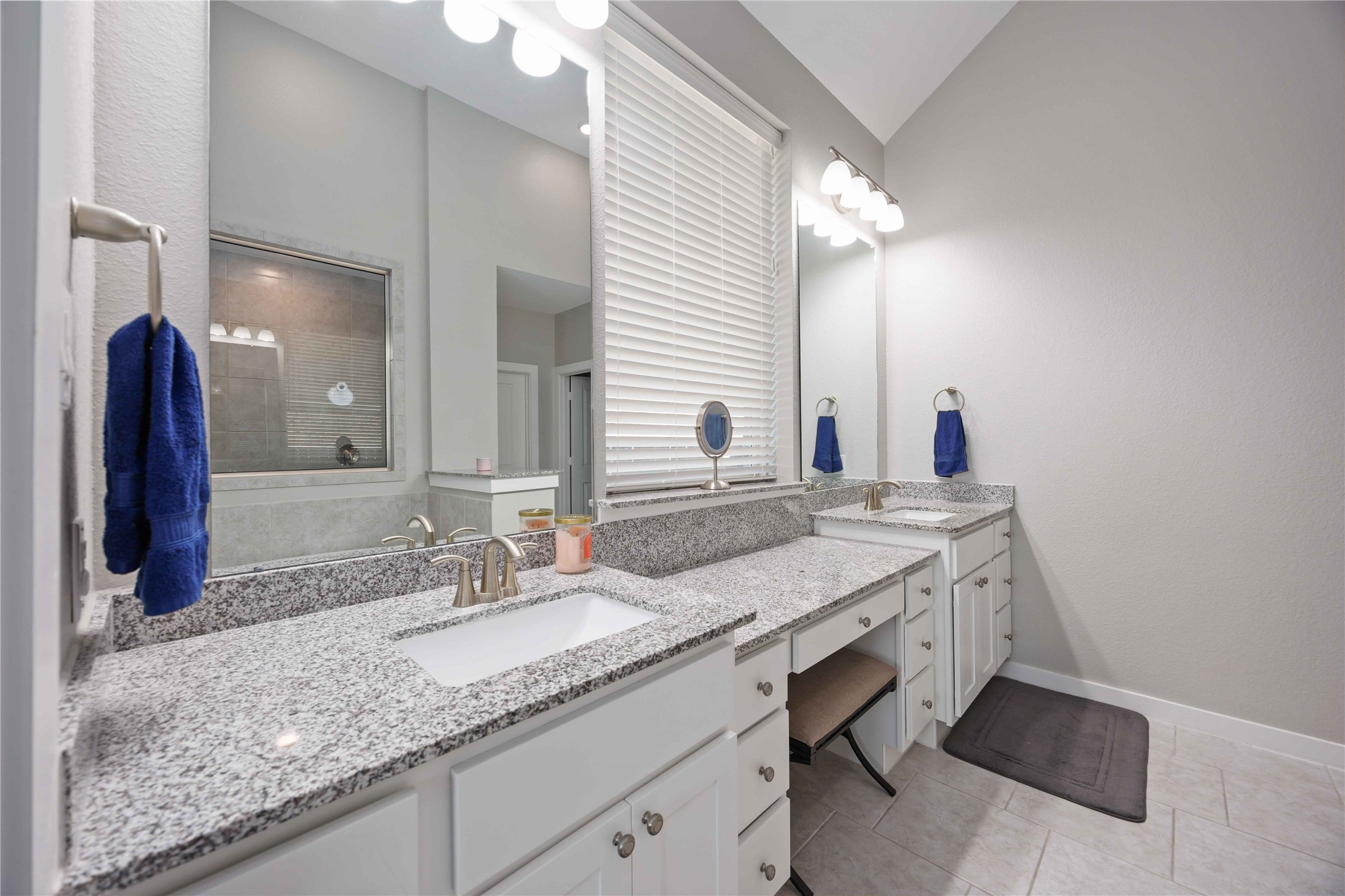 This bathroom features dual sinks with granite countertops, ample cabinet space, and a large mirror with modern lighting. The neutral tile flooring and soft wall colors create a clean, inviting atmosphere.
