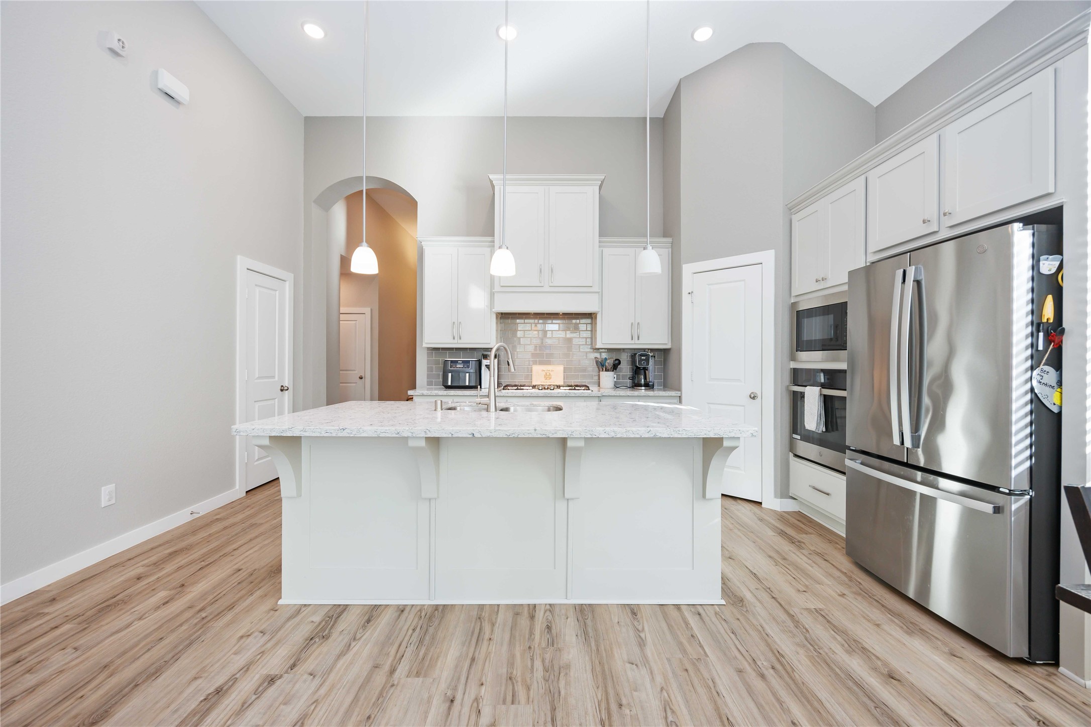 This kitchen features a spacious, modern design with high ceilings and ample lighting. It includes a large island with a marble countertop, stainless steel appliances, and sleek white cabinetry for a clean, elegant look. This kitchen features a spacious, modern design with high ceilings and ample lighting. It includes a large island with a marble countertop, stainless steel appliances, and sleek white cabinetry for a clean, elegant look.