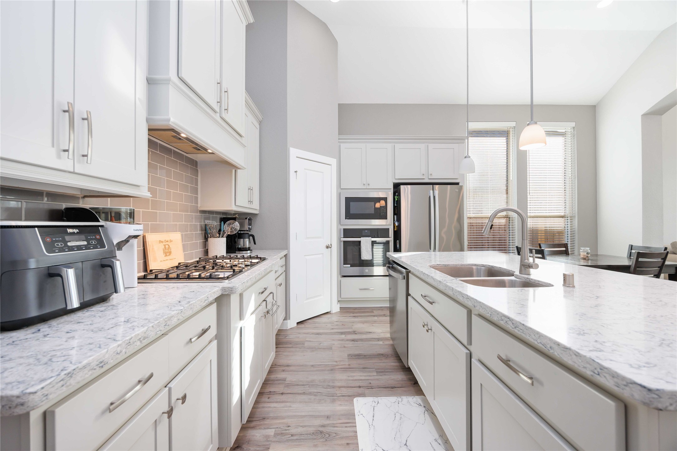 This modern kitchen features sleek white cabinetry, granite countertops, and stainless steel appliances. It includes a spacious island with a double sink, pendant lighting, and a gas stove, offering a bright, open feel with ample natural light. This modern kitchen features sleek white cabinetry, granite countertops, and stainless steel appliances. It includes a spacious island with a double sink, pendant lighting, and a gas stove, offering a bright, open feel with ample natural light.