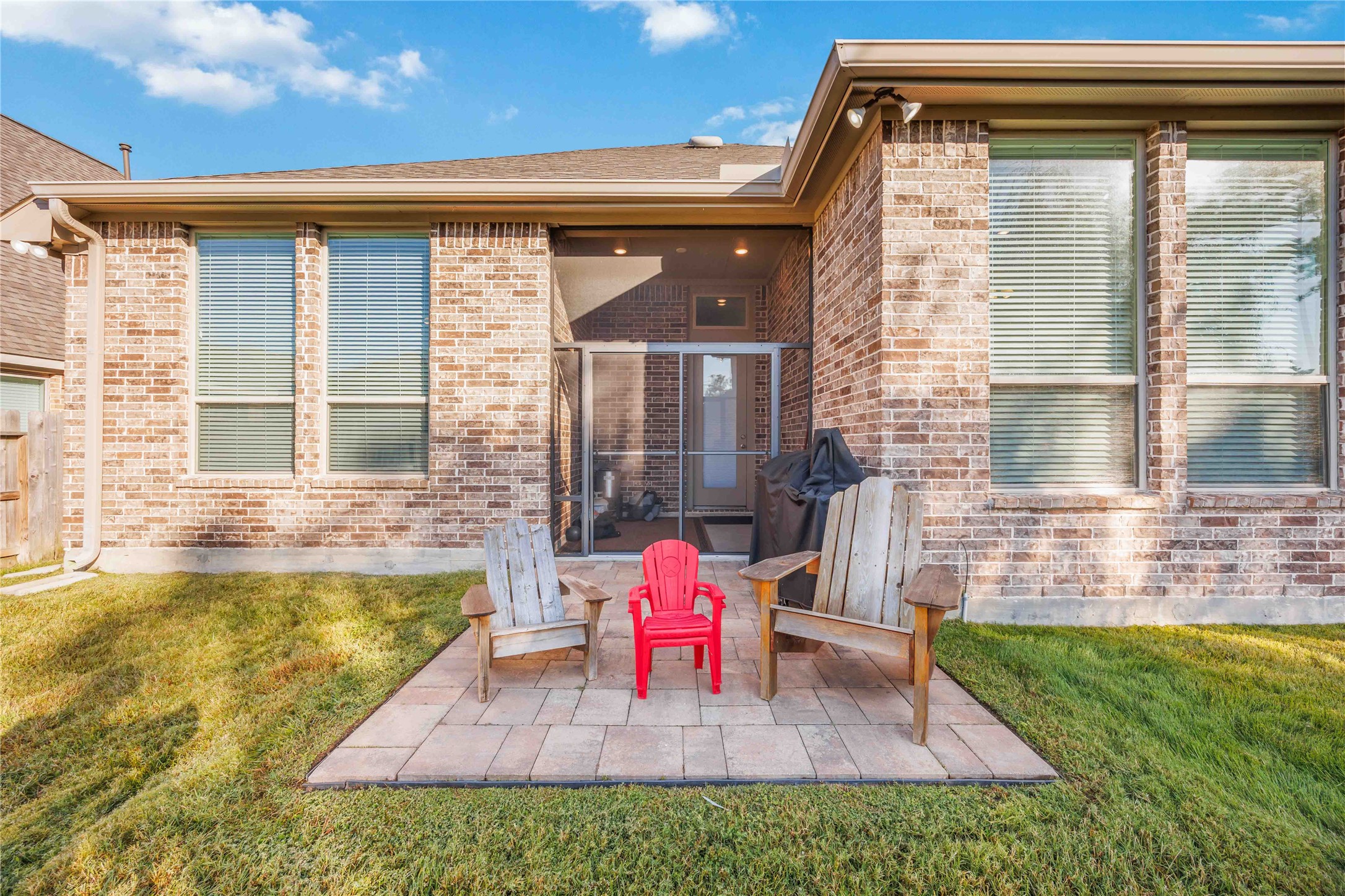 Charming brick patio with two wooden chairs and a child's chair, perfect for relaxing. The backyard features a well-maintained lawn and a covered entryway, ideal for outdoor enjoyment.
