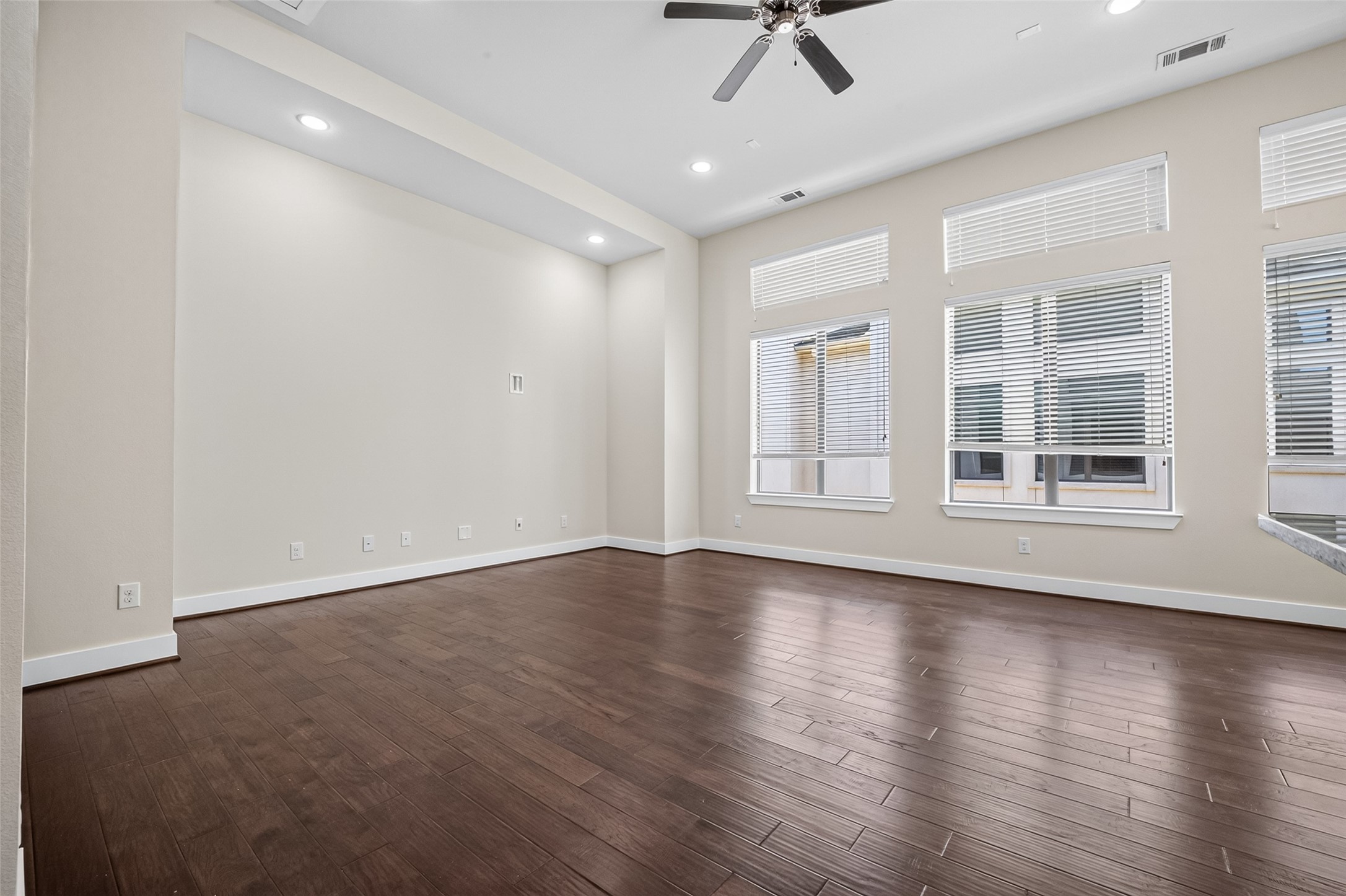 Spacious living area with rich hardwood floors, large windows for ample natural light, and a modern ceiling fan for comfort.