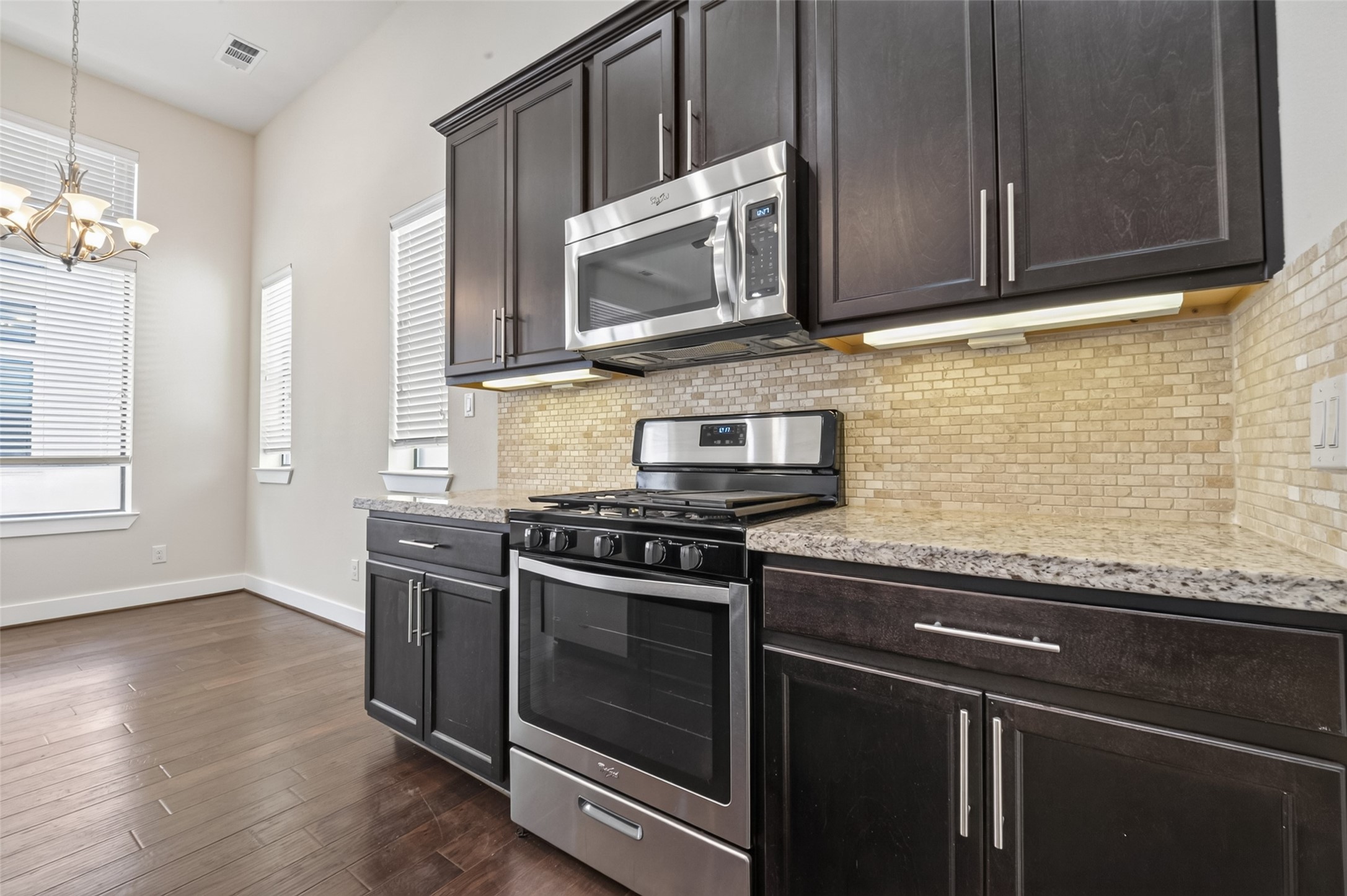 Modern kitchen with sleek dark cabinets, stainless steel appliances, and a stylish tile backsplash, complemented by warm hardwood floors and ample natural light.