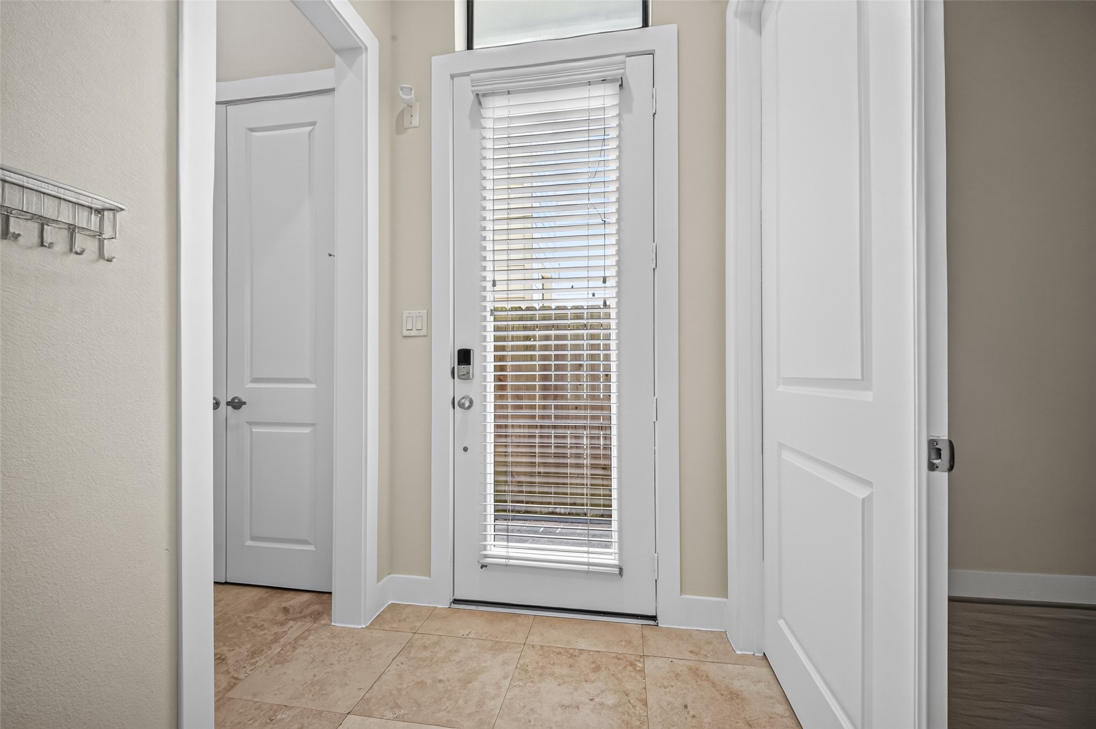 Inviting entryway with a glass door featuring blinds, neutral tile flooring, and ample natural light.