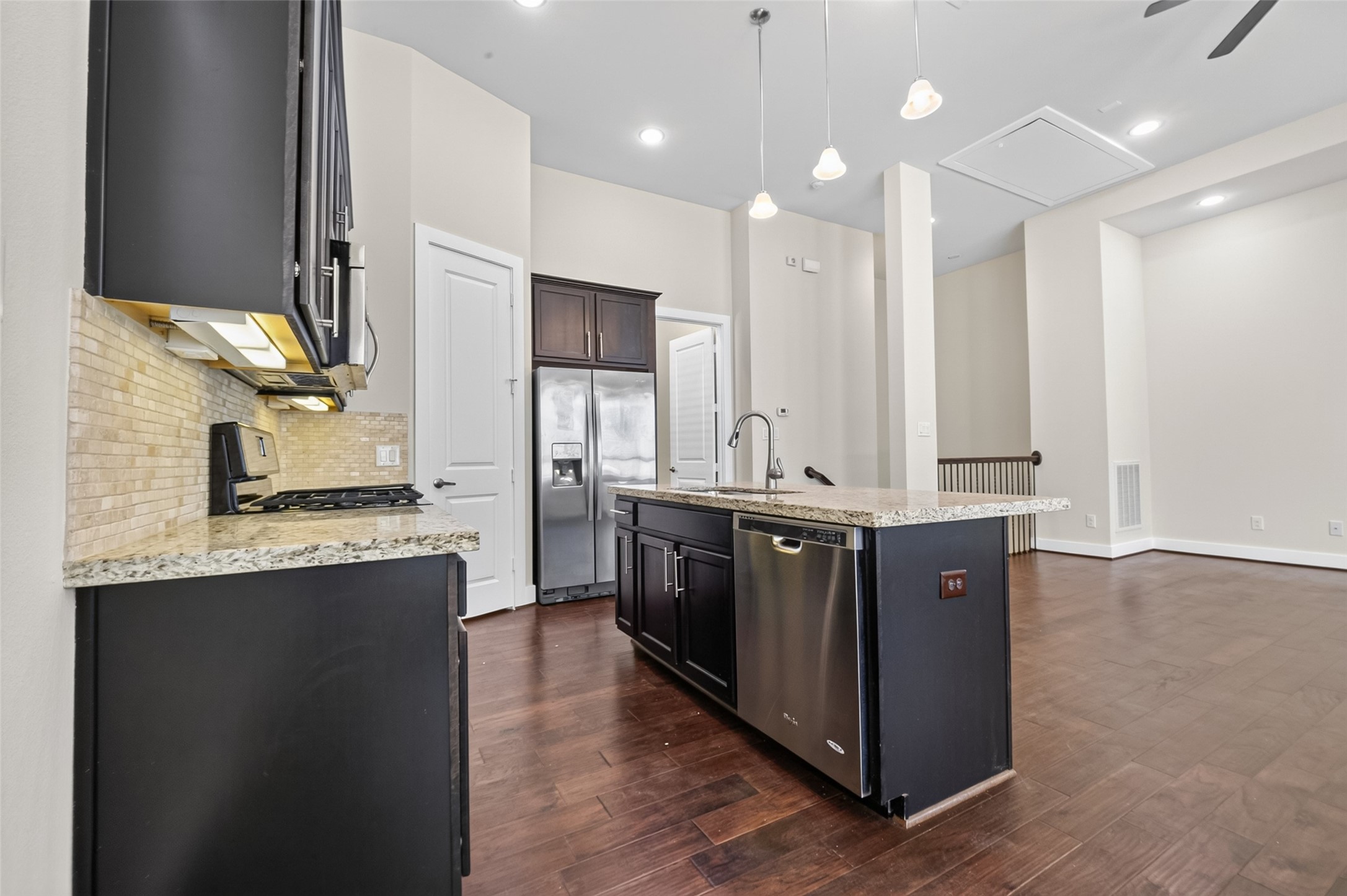 Spacious kitchen with sleek dark cabinetry, granite countertops, and modern stainless steel appliances, seamlessly opening into a bright living area with elegant hardwood floors.