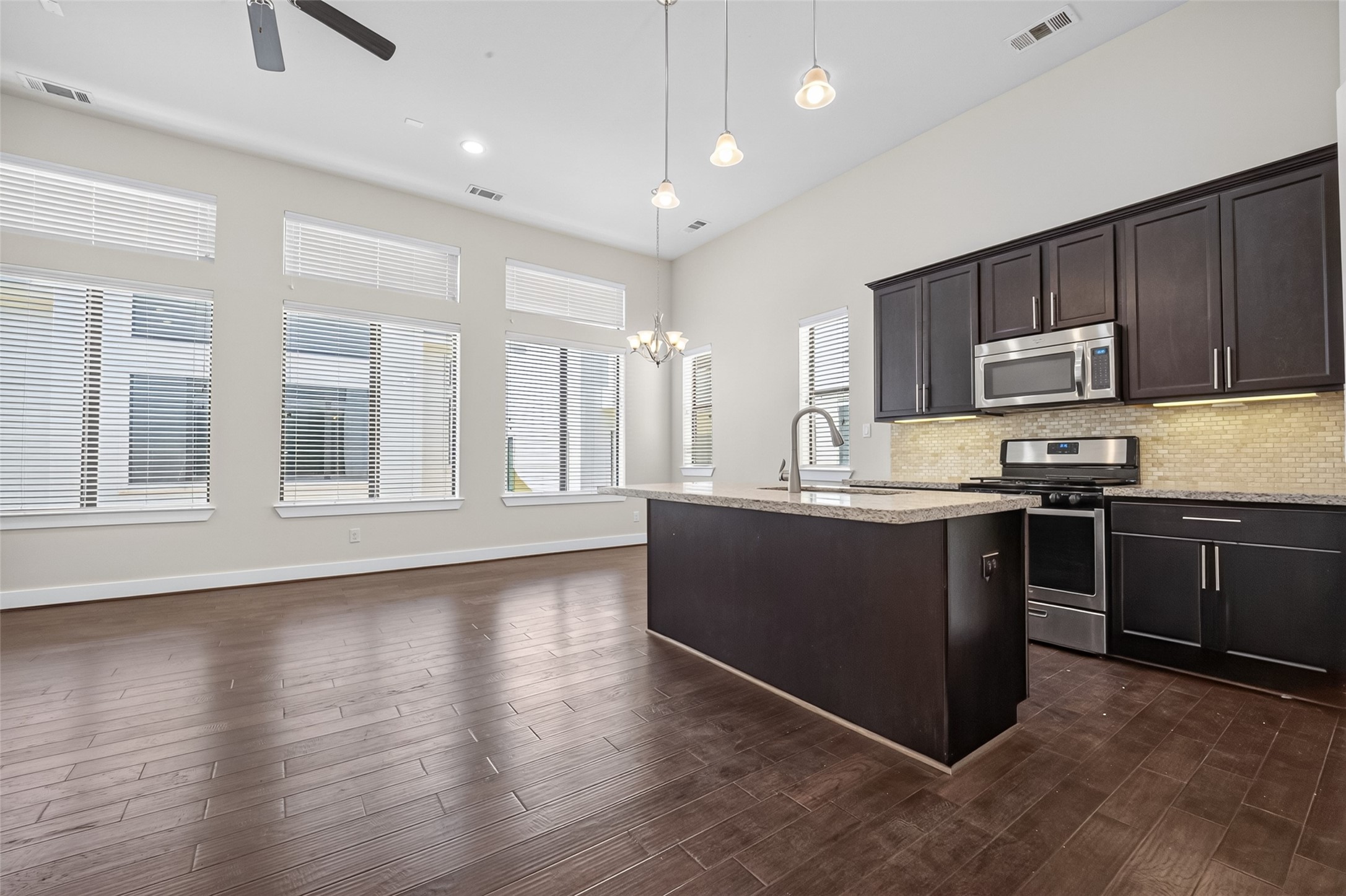 Spacious open-concept kitchen and living area featuring high ceilings, abundant natural light, sleek dark cabinetry, and modern stainless steel appliances.