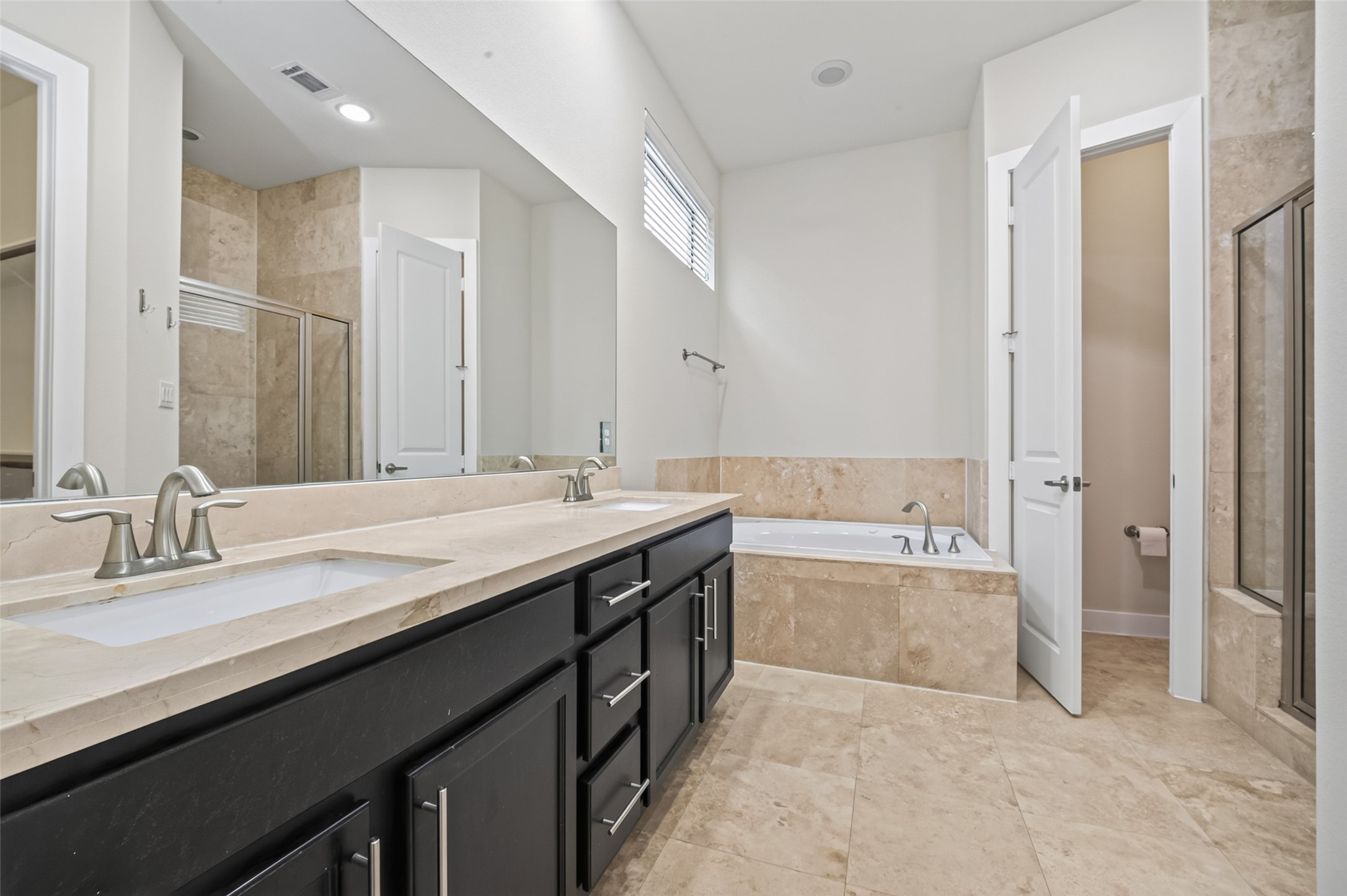 Luxurious bathroom featuring a double vanity with elegant fixtures, a spacious soaking tub, and a separate glass-enclosed shower, all accented with sleek tile flooring and modern finishes.