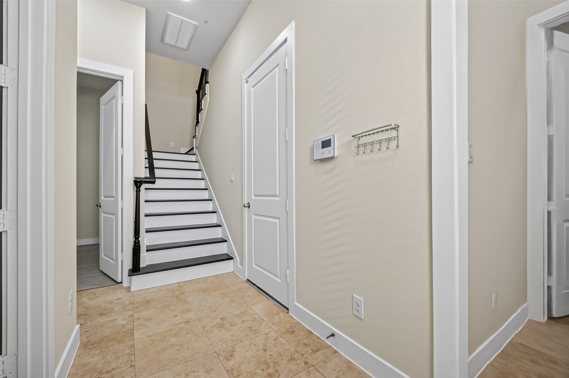 Inviting entryway with elegant tile flooring leads to a staircase featuring dark wood accents, complemented by neutral walls and modern finishes.