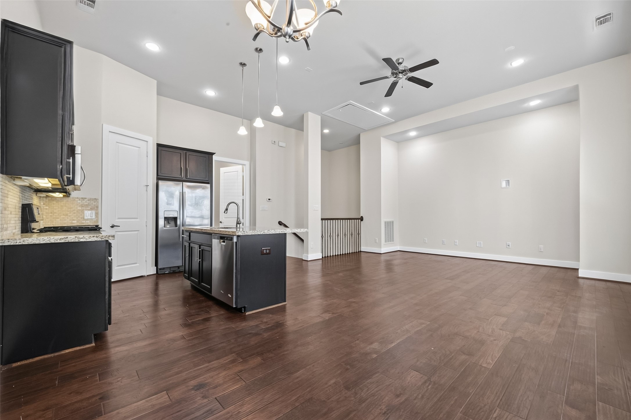 Spacious open-concept living area with elegant hardwood floors and a modern kitchen featuring dark cabinetry, granite countertops, and stainless steel appliances.