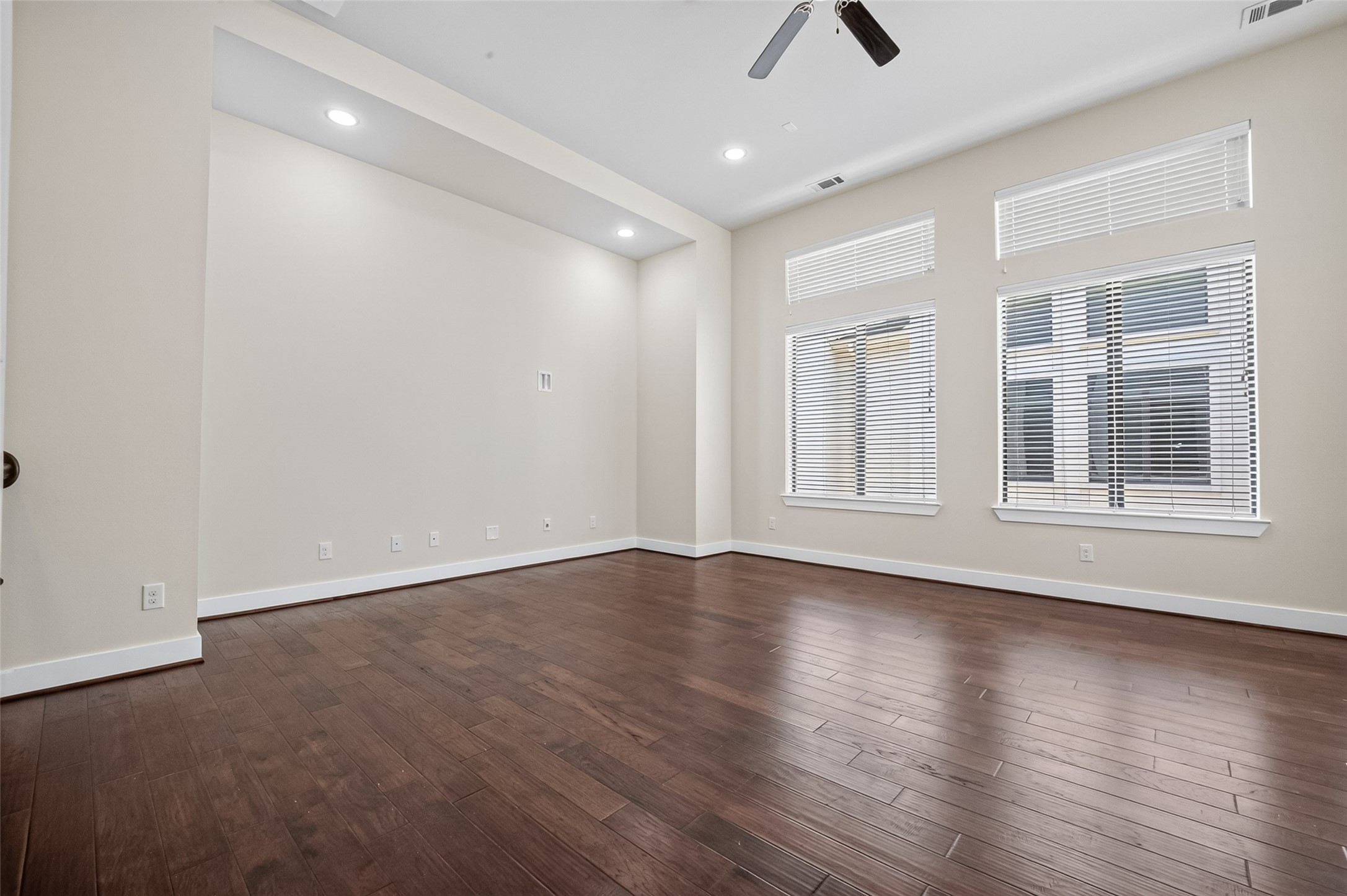 Spacious room with rich hardwood floors, large windows offering ample natural light, and modern recessed lighting.
