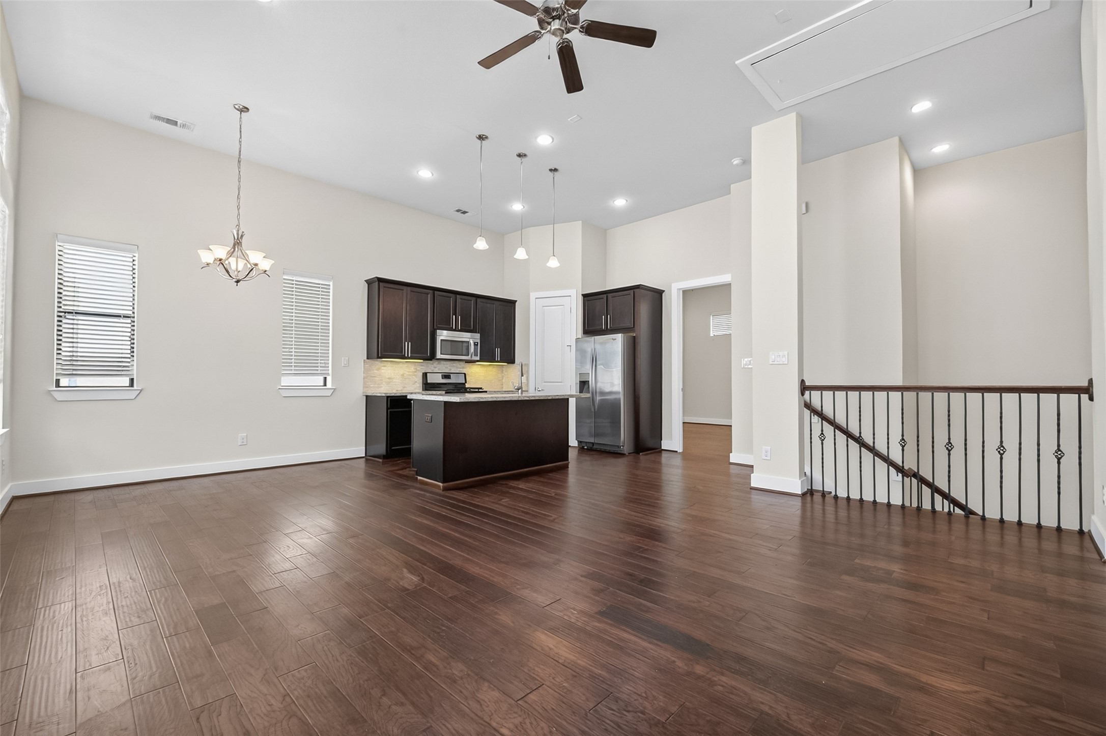 Spacious open-concept living area featuring rich hardwood floors, a modern kitchen with stainless steel appliances, and elegant lighting fixtures, perfect for entertaining.