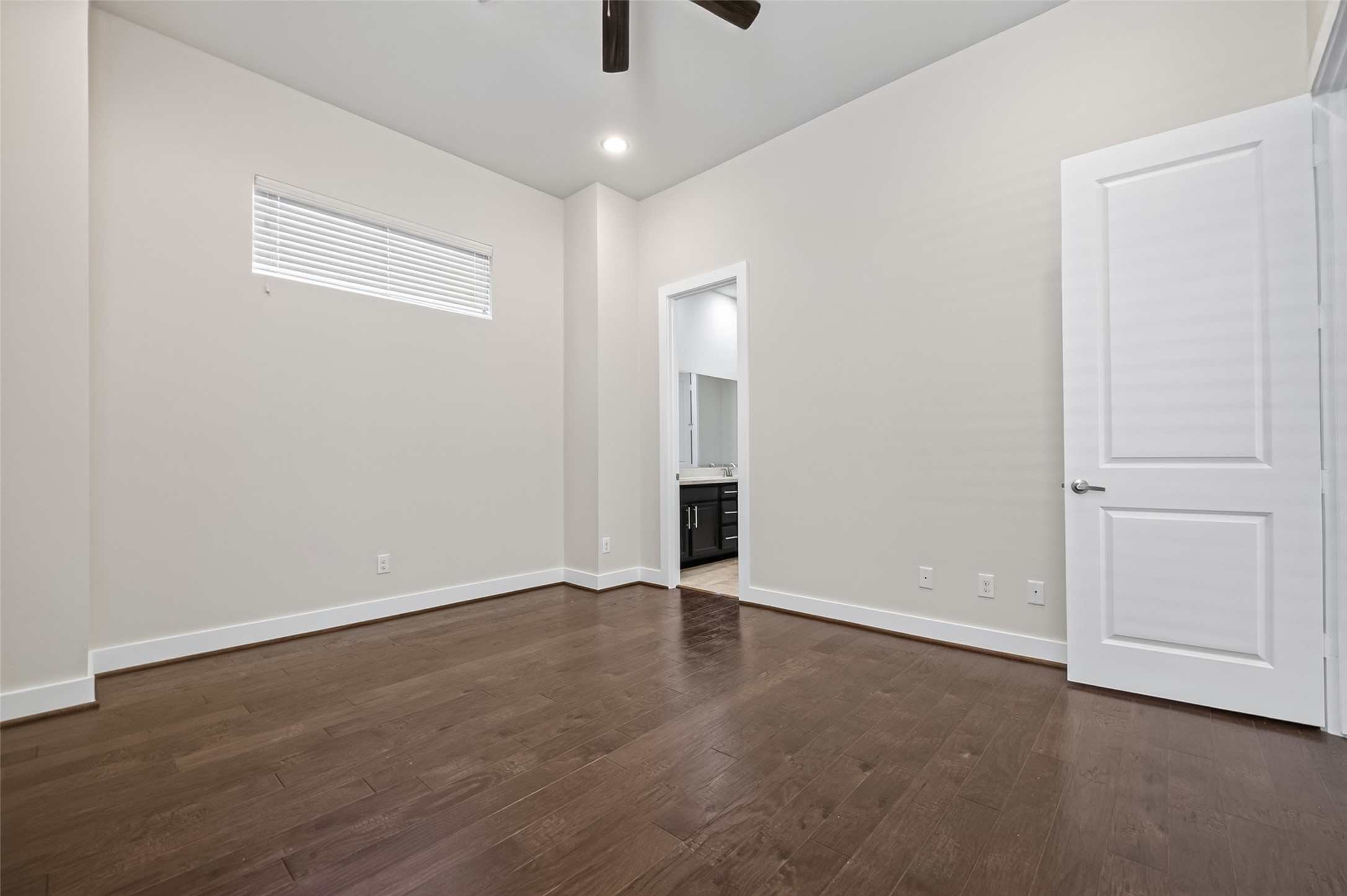 Spacious bedroom with hardwood floors, neutral walls, and a ceiling fan, leading to an en-suite bathroom.