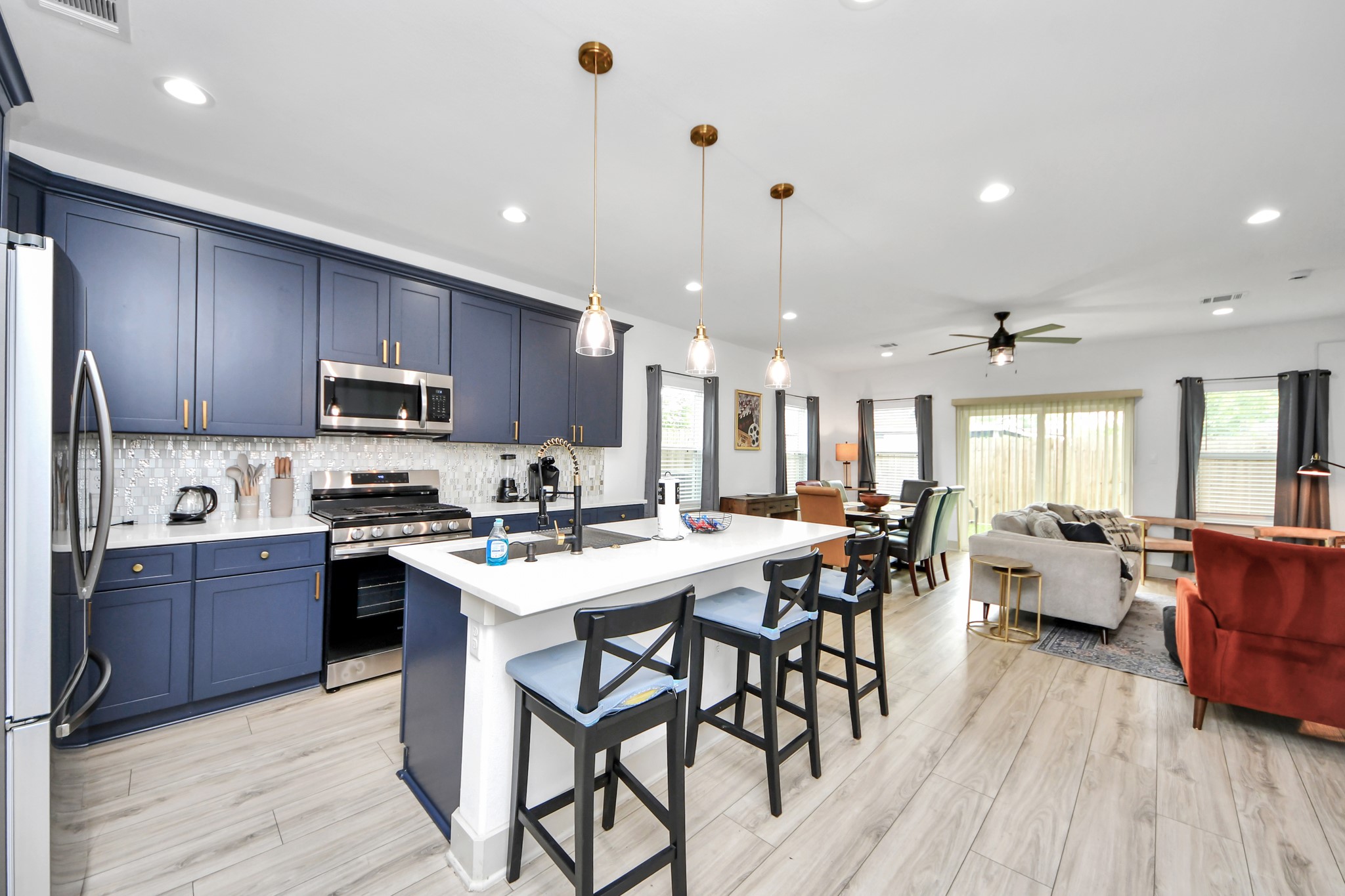 Bright open-concept kitchen with deep blue cabinetry, stainless steel appliances, large center island, and pendant lighting.