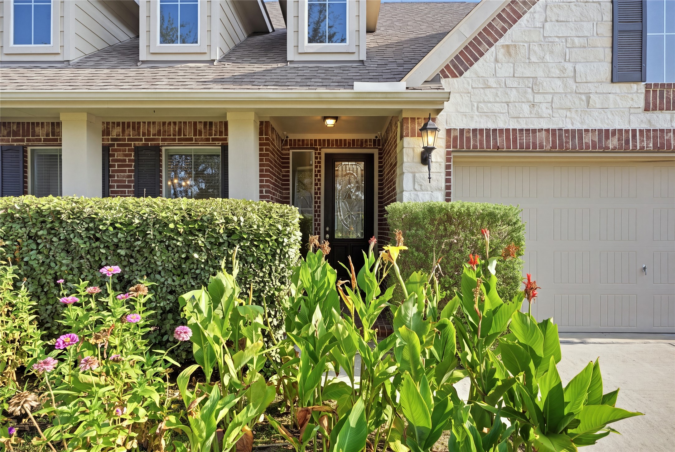 The covered front porch is surrounded by lush landscaping and leads to a decorative glass front door, creating an inviting entrance to the home.