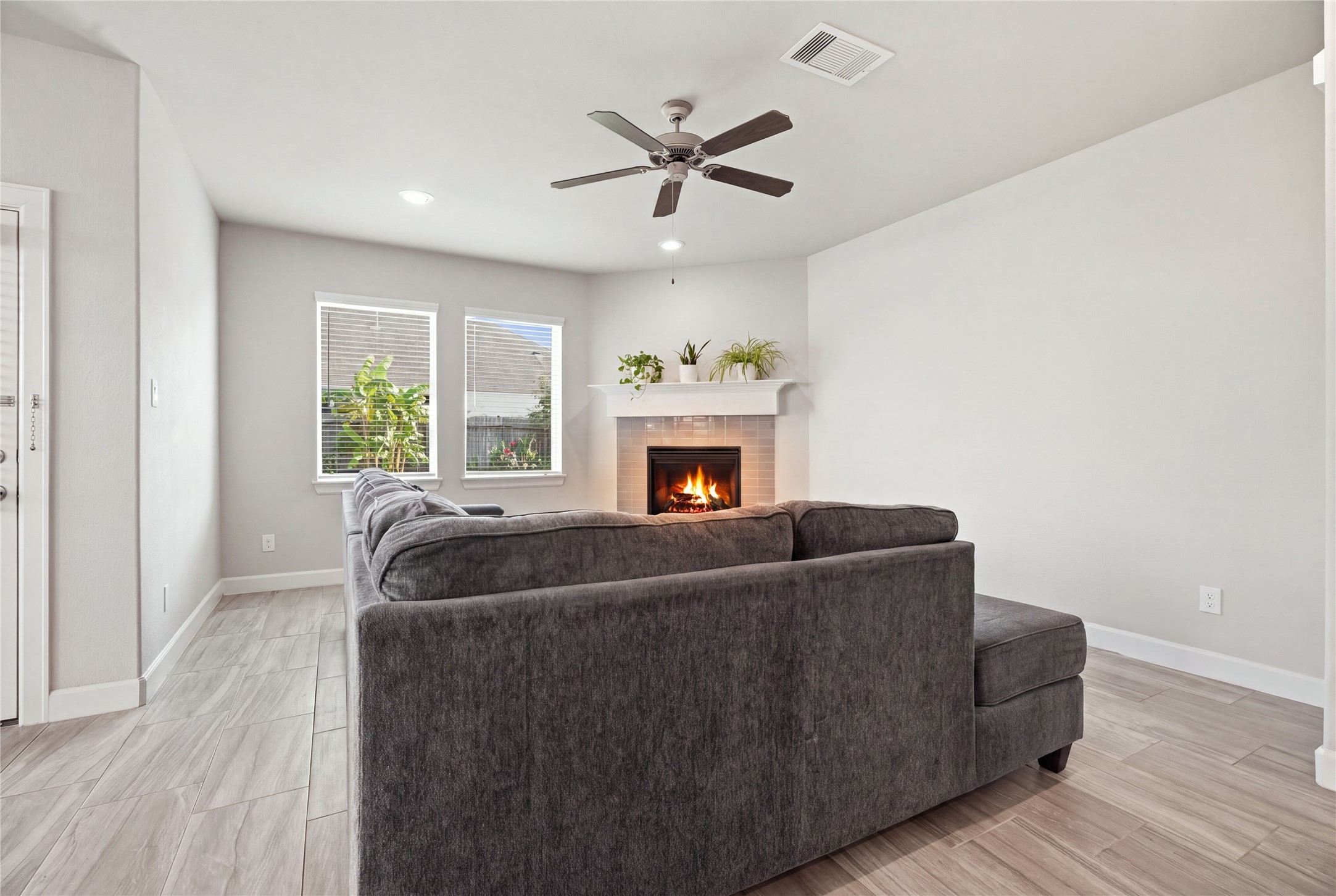 Inviting living room featuring tile flooring, a fireplace, recessed lighting, ceiling fan, and windows overlooking the backyard.