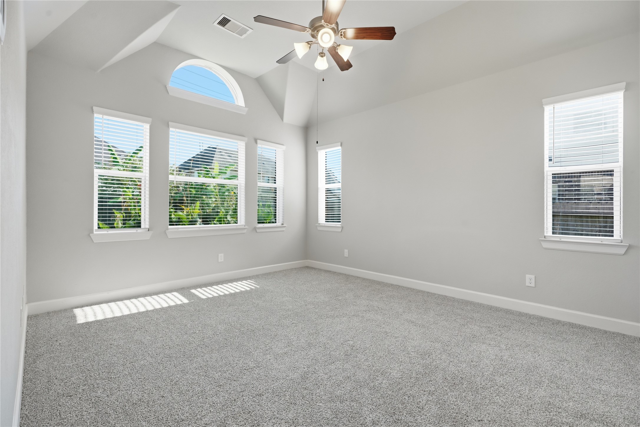 Spacious primary bedroom featuring carpet replaced in August 2026 and a wall of windows that fills the room with natural light and offers views of the backyard.