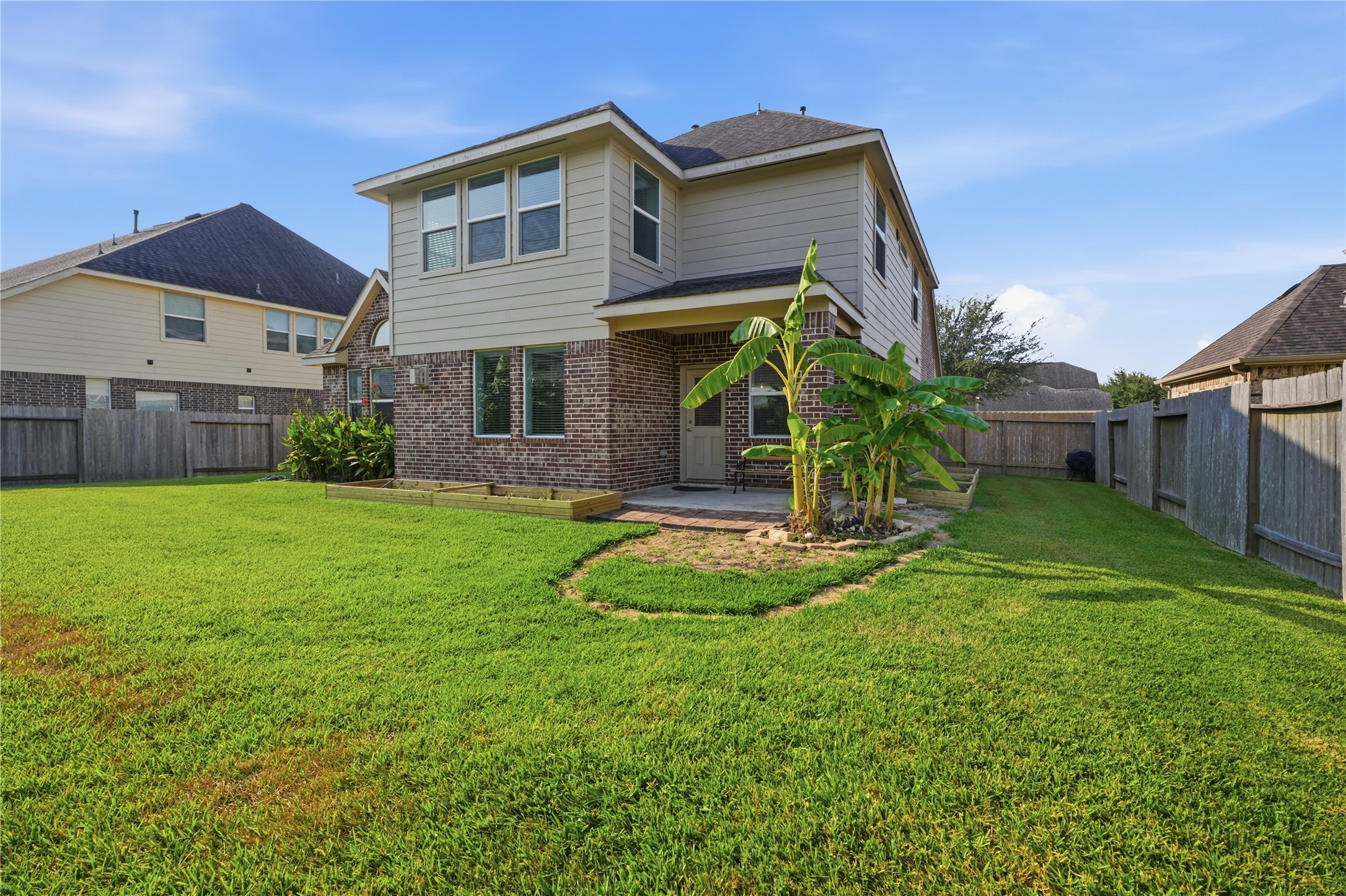 Rear view of the home showcases the covered patio, expansive fenced yard, and freshly prepared garden beds along the back of the home.