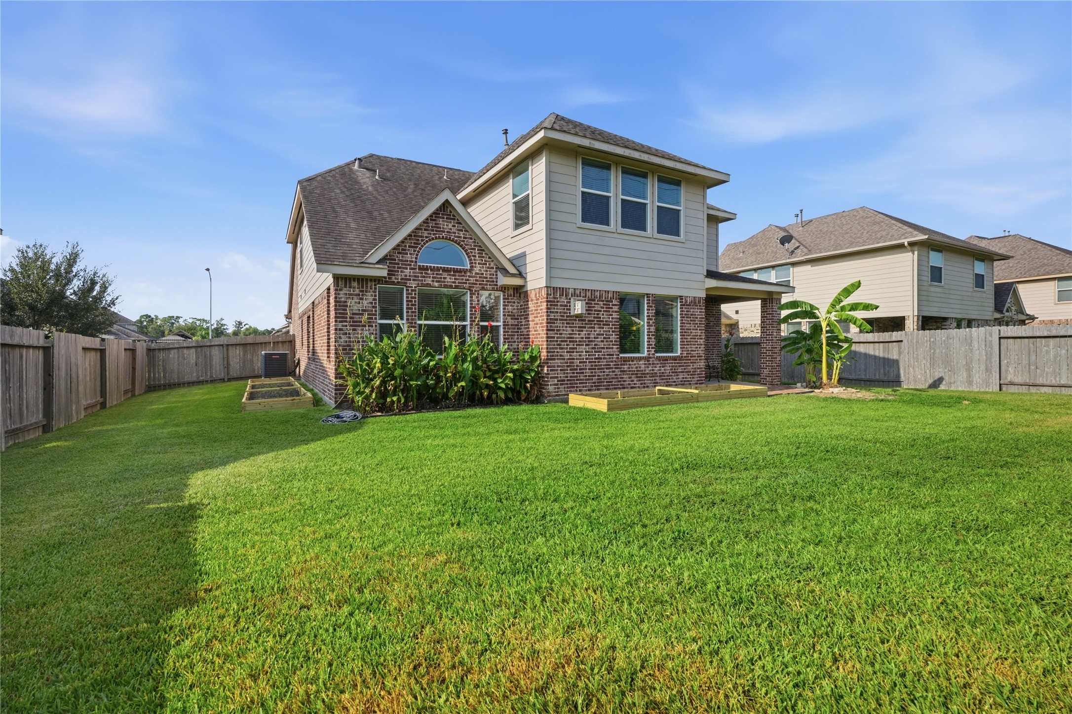 Spacious fenced backyard with a large grassy area, mature landscaping, and freshly prepared garden beds ready for planting.