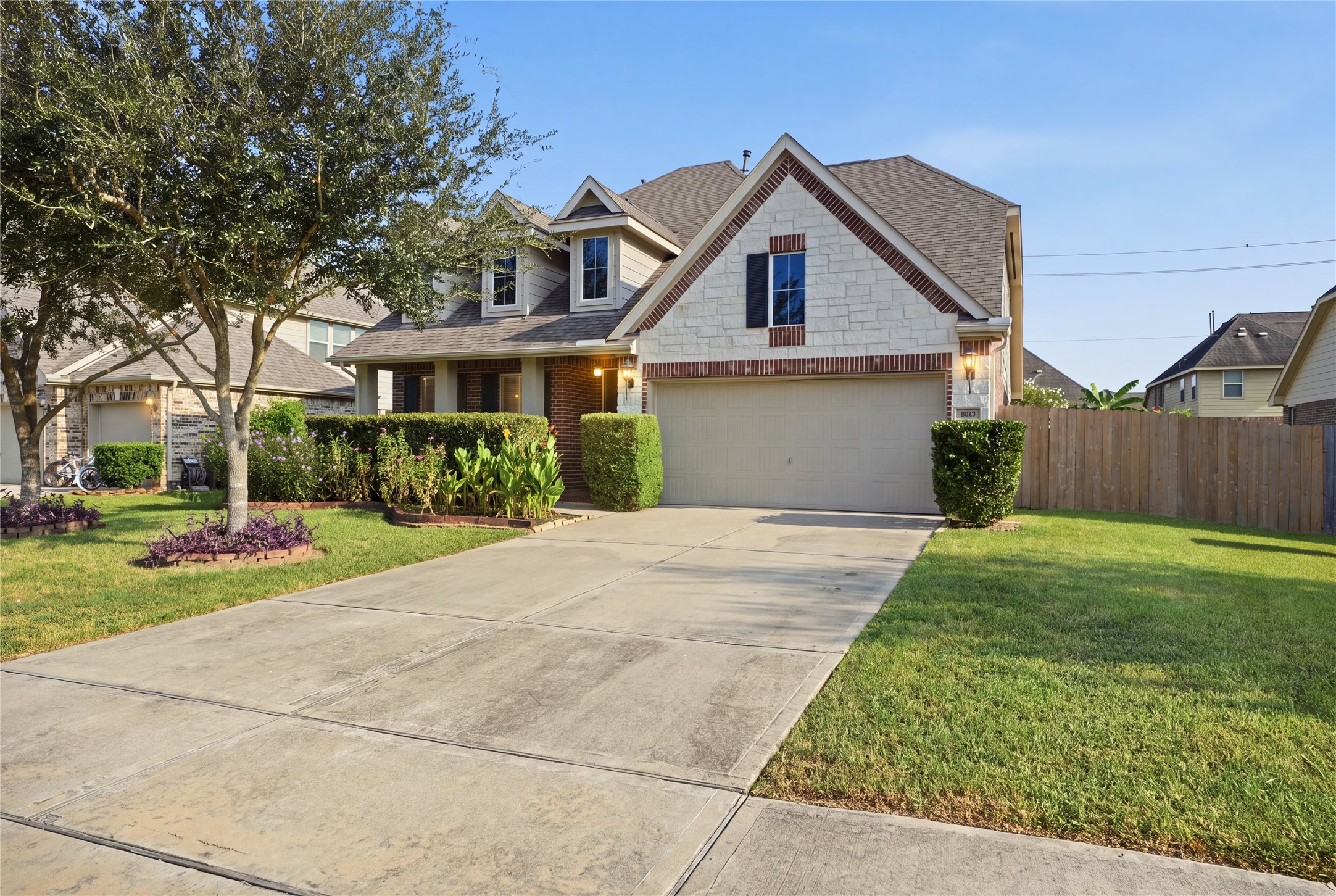 A closer look at the homes inviting exterior, featuring a spacious driveway, two-car garage, mature landscaping, and a covered front porch.