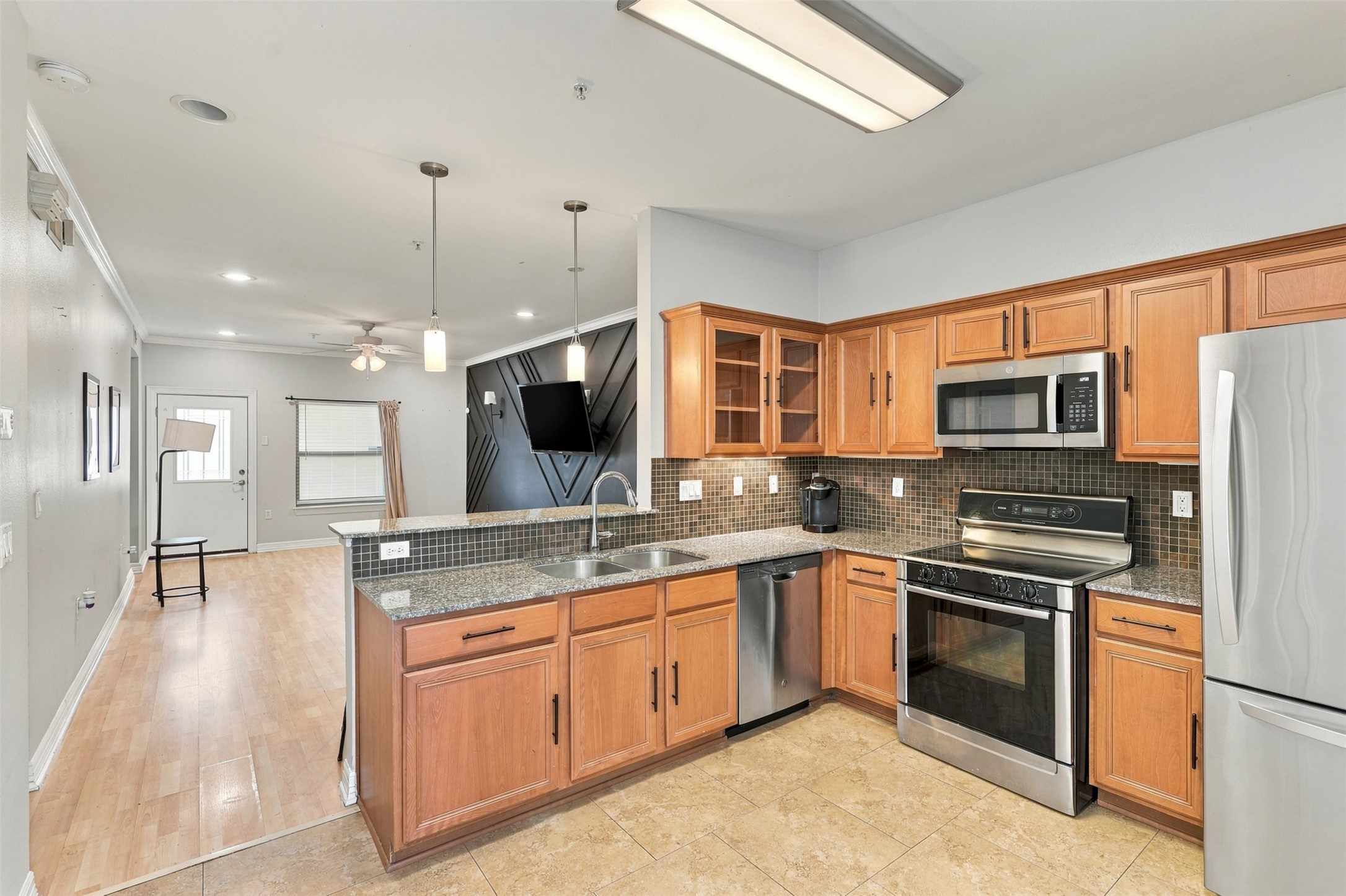 Modern kitchen with stainless steel appliances, elegant wood cabinetry, and stylish tile backsplash, seamlessly connecting to an open living area with hardwood floors and contemporary lighting.