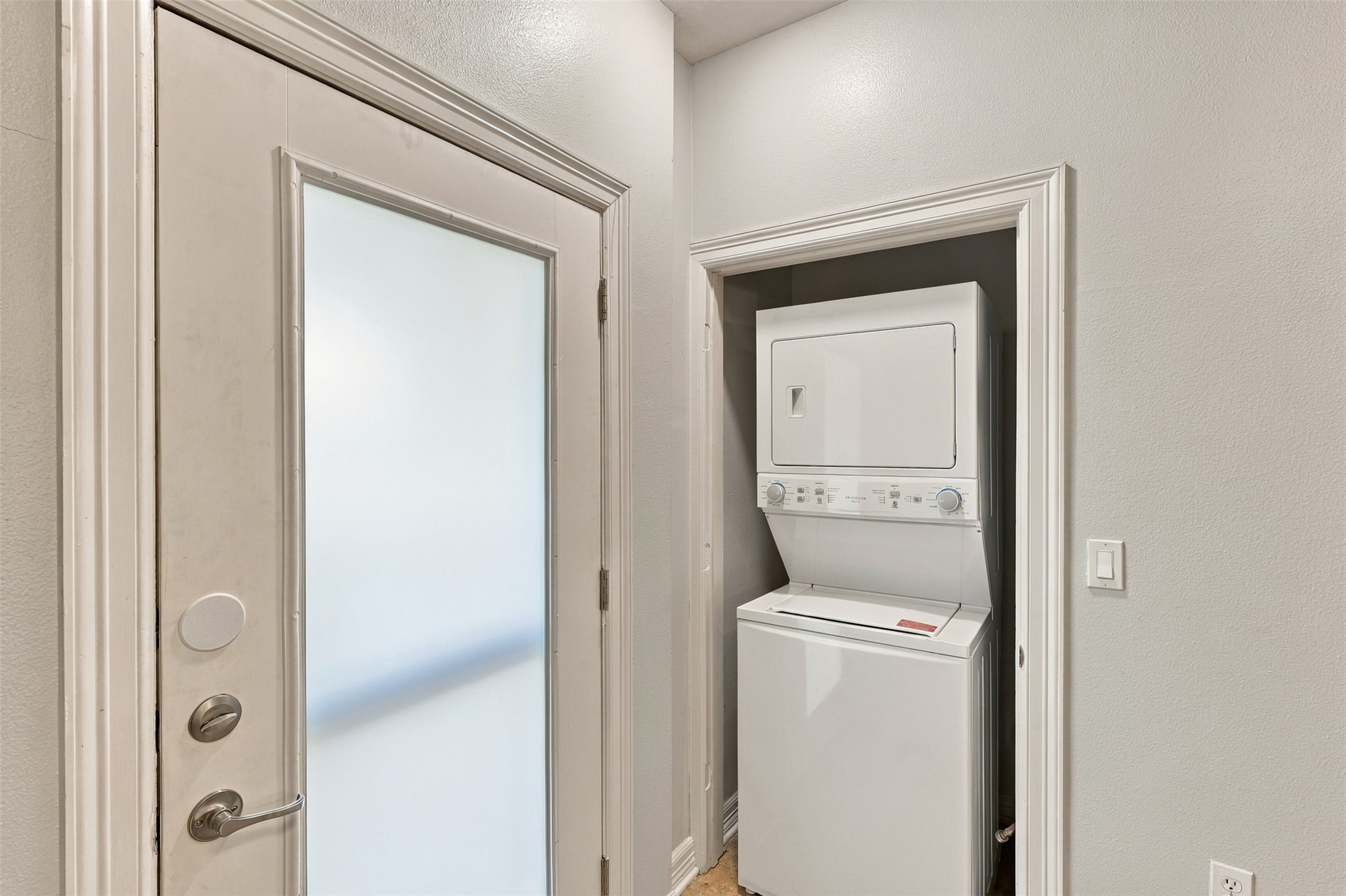 Convenient laundry nook with a stacked washer and dryer set, situated next to a frosted glass door for added privacy.