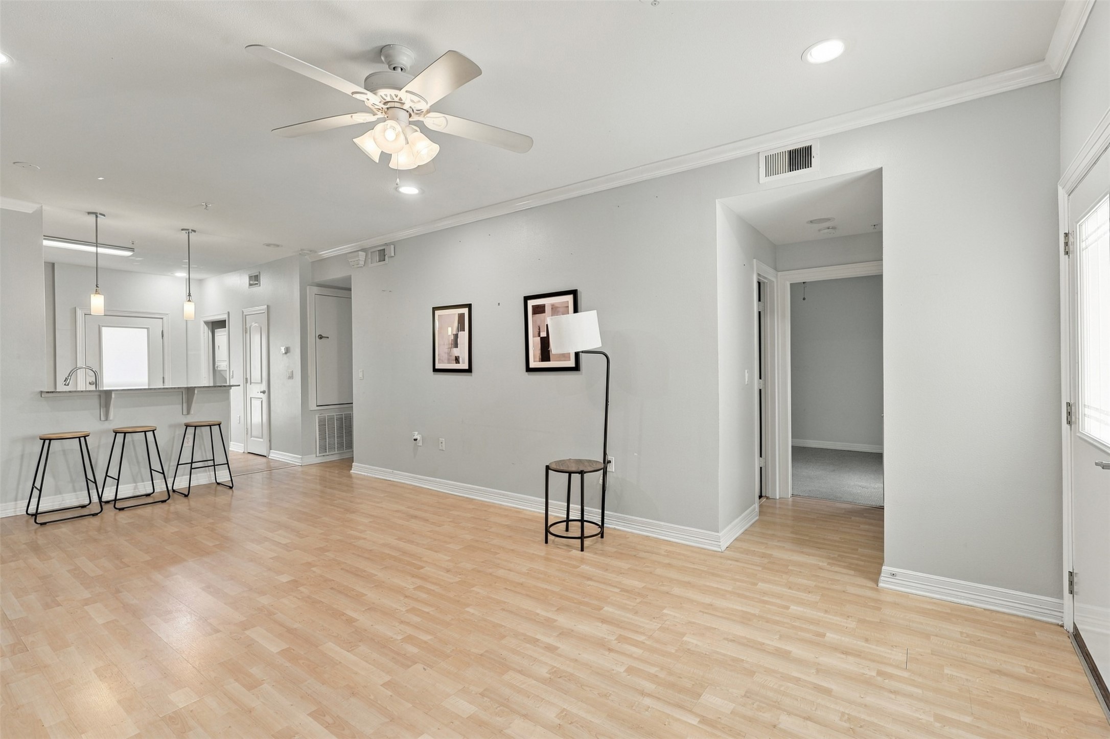 Spacious open-concept living area with light wood flooring, featuring a breakfast bar with modern pendant lighting and comfortable seating, ideal for entertaining.