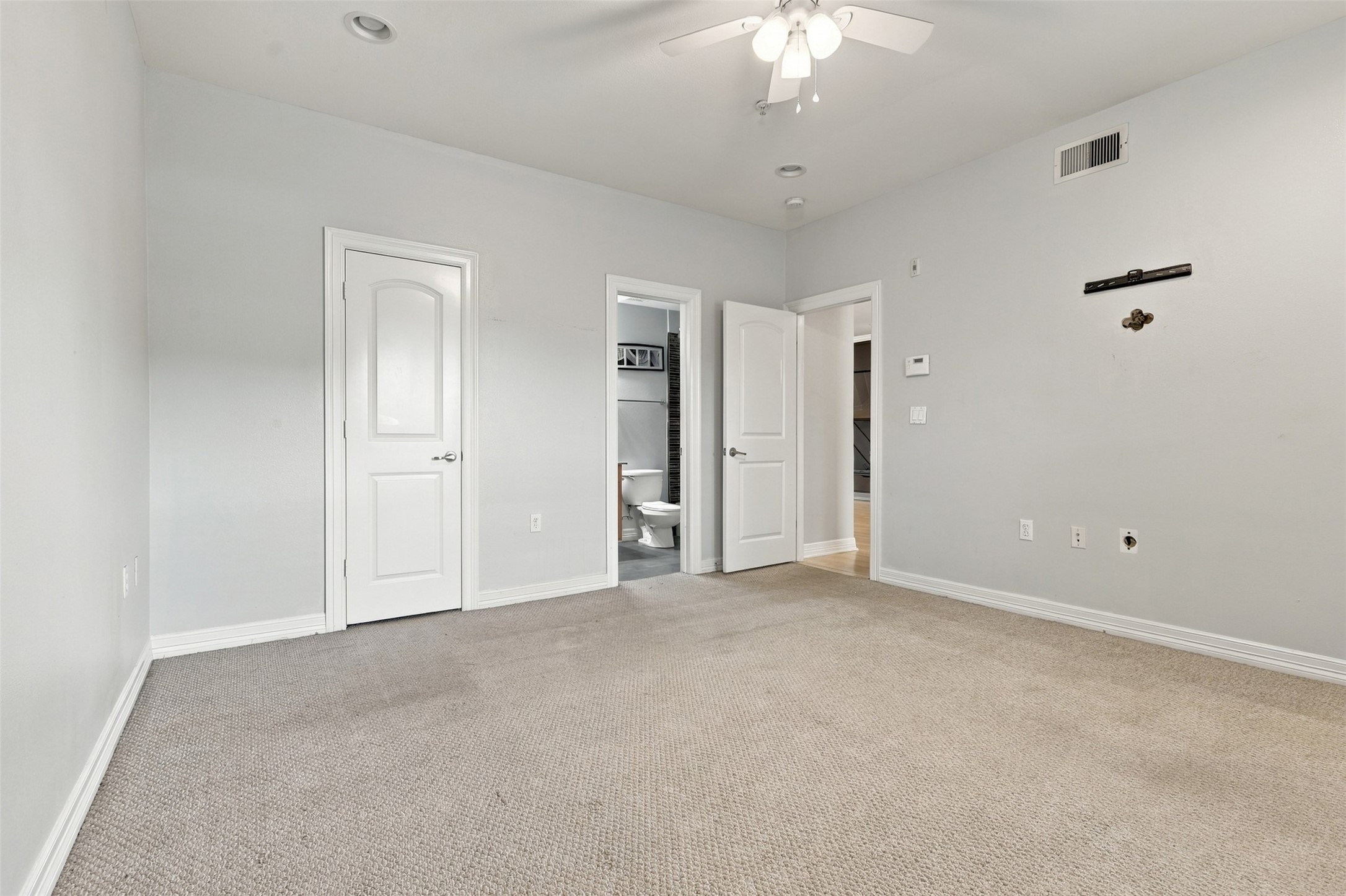 Spacious bedroom with neutral walls and carpet, featuring a ceiling fan and en-suite bathroom access for added convenience.