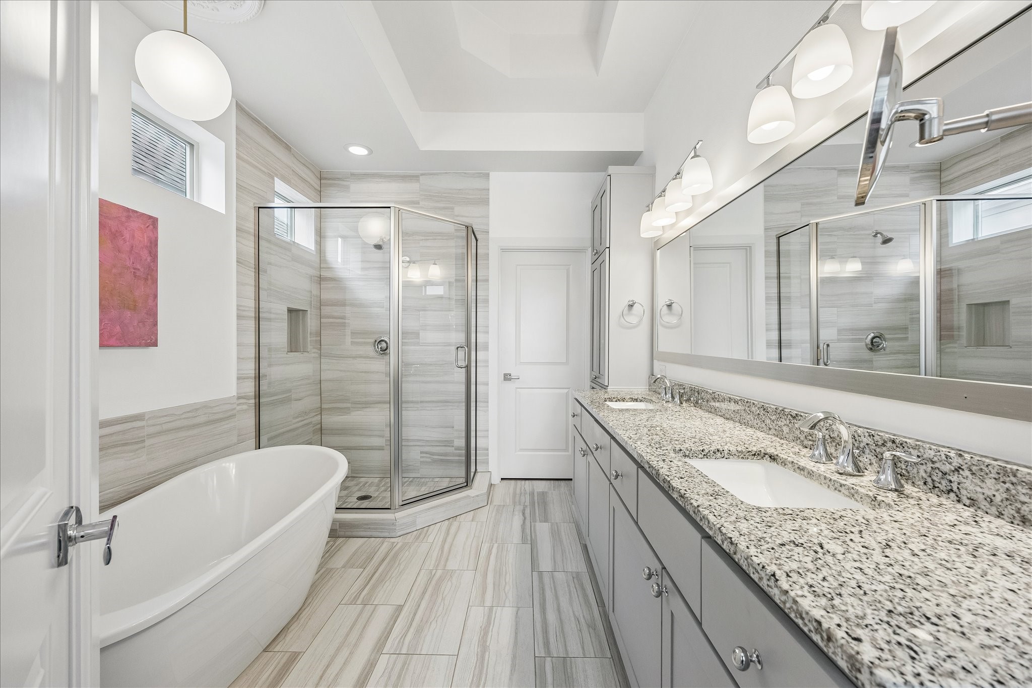 Dreamy primary bath featuring expansive vanity w/ dual sinks, beautiful granite countertops & abundant cabinetry for storage! Decorative vanity lighting & large mirror enhance the thoughtfully designed space. Glass-front storage cabinets w/ additional cabinetry below provide excellent organization. Separate walk-in closet offers wonderful additional storage & functionality!