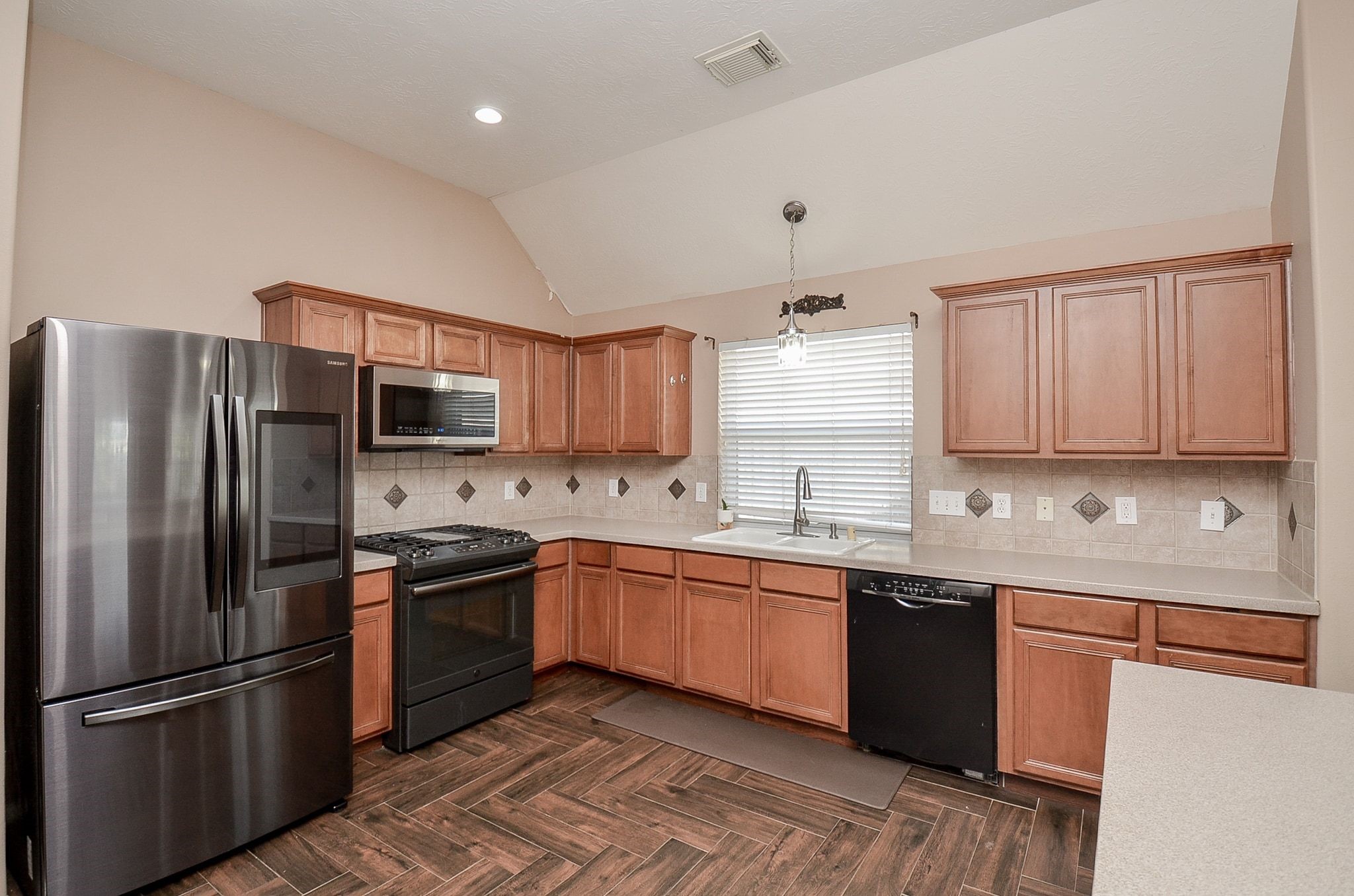 Spacious kitchen featuring sleek stainless steel appliances, warm wood cabinetry, and elegant tile backsplash, complemented by rich wood tile flooring and ample counter space.