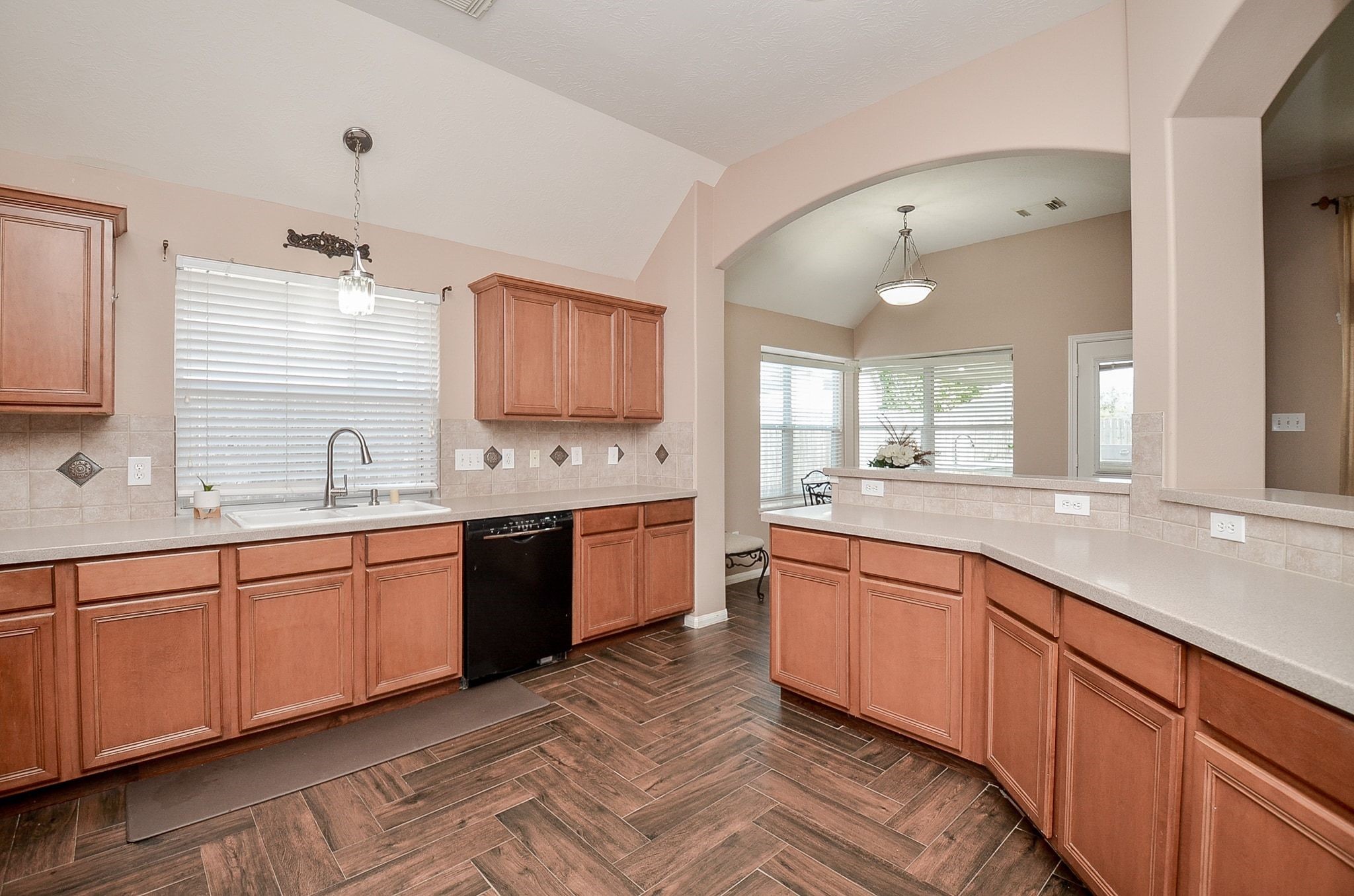 Spacious kitchen with elegant wooden cabinetry, sleek countertops, and a stylish tile floor, featuring a large window for natural light and an open view into the dining area.