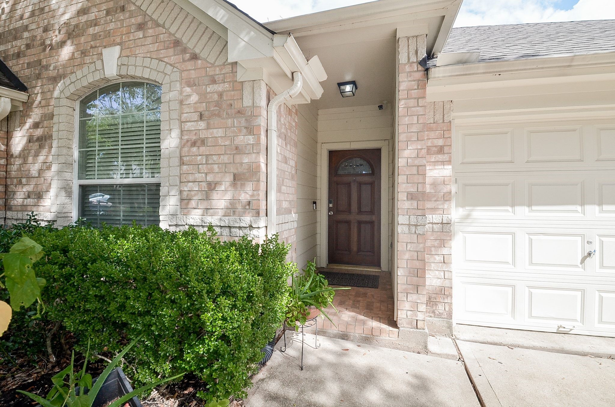 Charming brick exterior with inviting entryway, complemented by lush greenery and a classic garage door.