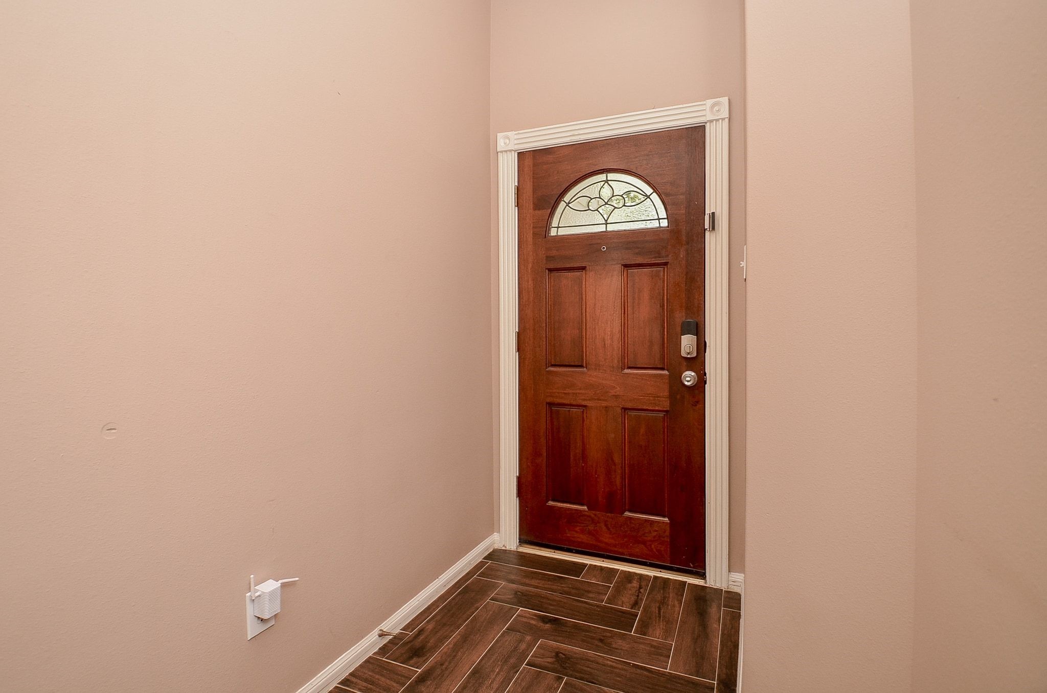 Inviting entryway with a rich wooden door featuring an elegant glass insert, complemented by warm-toned walls and stylish tile flooring.