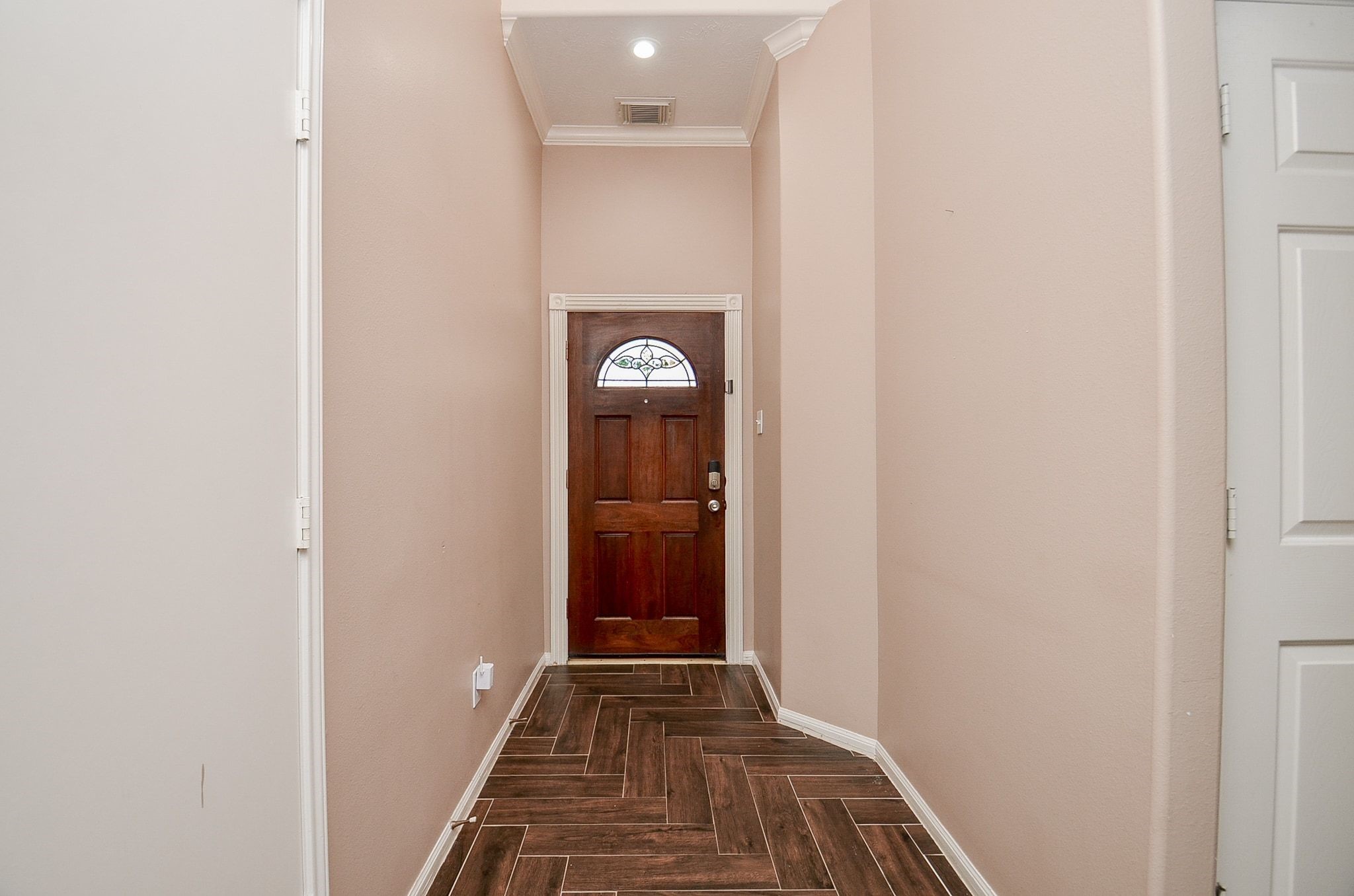 Inviting entryway with warm-toned walls, elegant crown molding, and stylish wood-look tile flooring leading to a charming wooden front door.