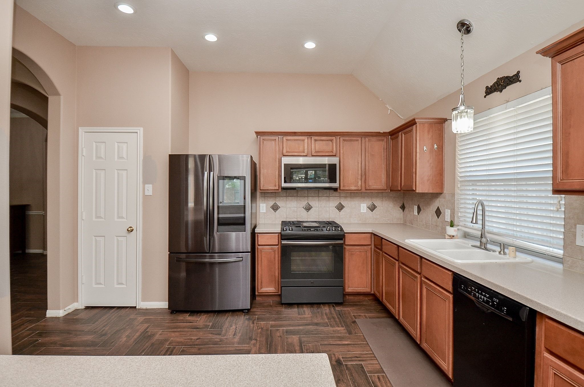 Spacious kitchen with stainless steel appliances, ample wooden cabinetry, and elegant tile backsplash. The large window provides plenty of natural light, complemented by recessed ceiling lighting.