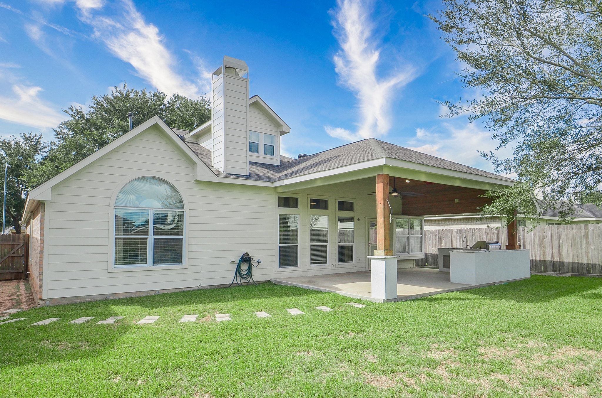 Charming backyard features a spacious covered patio with a built-in outdoor kitchen, perfect for entertaining, set against a backdrop of lush green lawn.