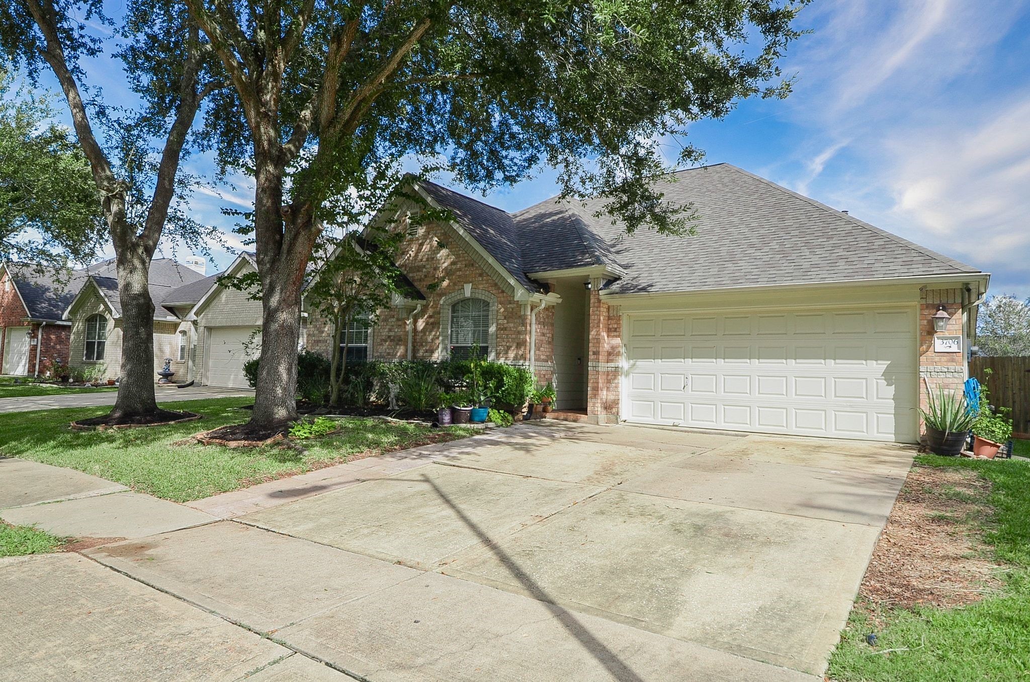 Charming brick home with a spacious two-car garage, nestled among mature trees and featuring a well-maintained front yard.