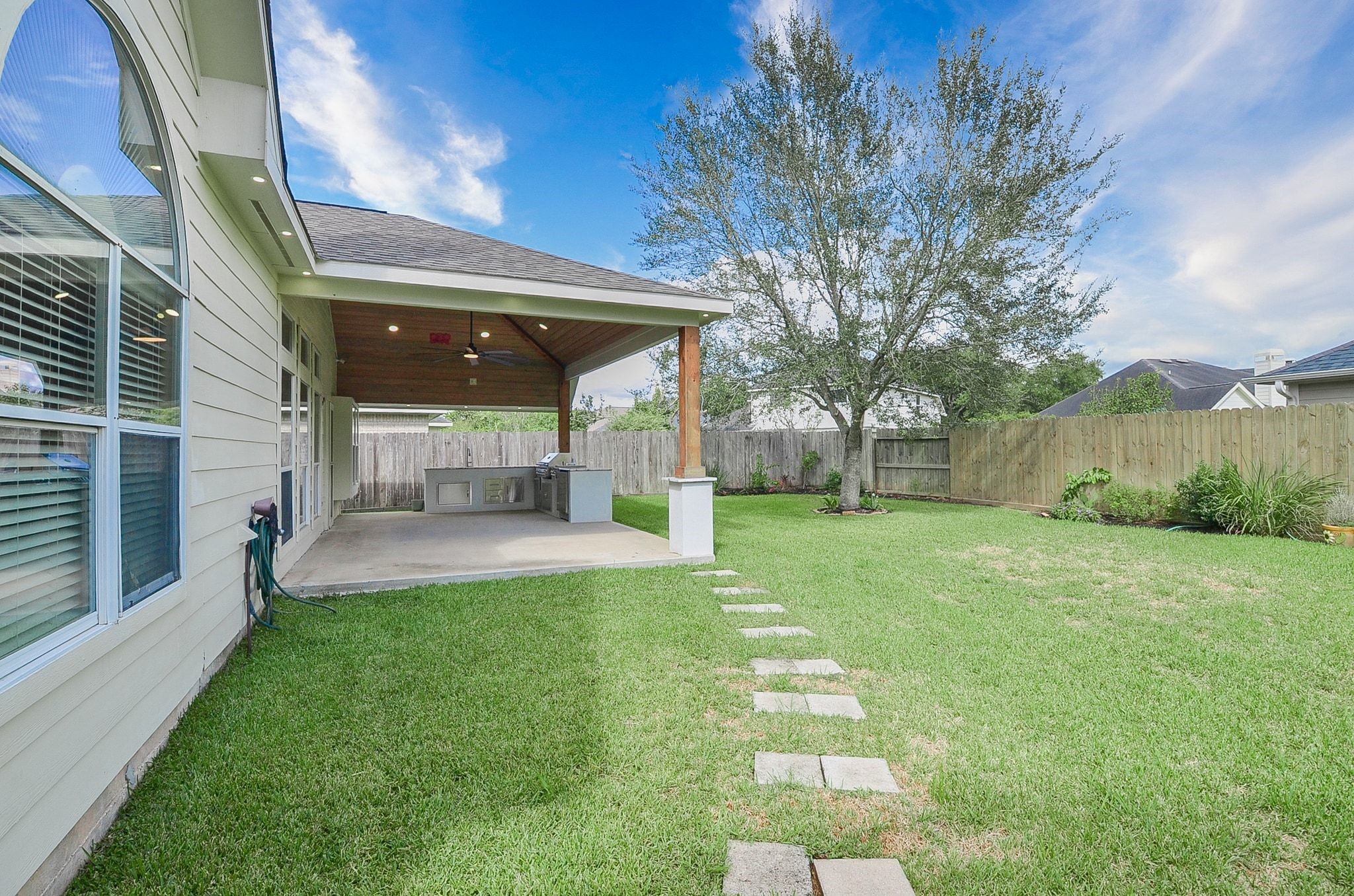Spacious backyard featuring a covered patio with an outdoor kitchen, perfect for entertaining, surrounded by a lush lawn and mature tree for added privacy.