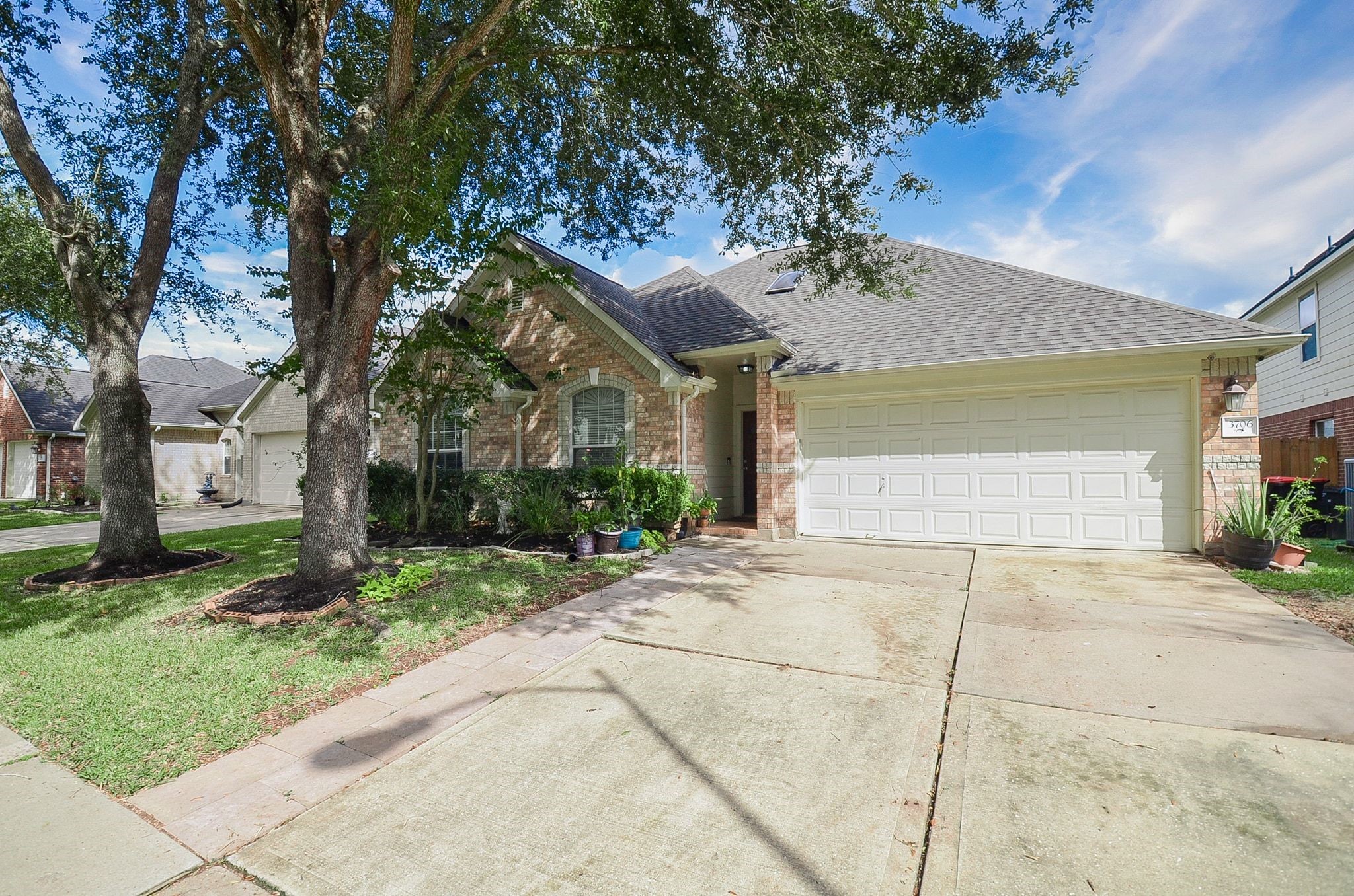 Charming brick home with a spacious two-car garage, nestled under mature trees, offering a welcoming front yard and inviting curb appeal.