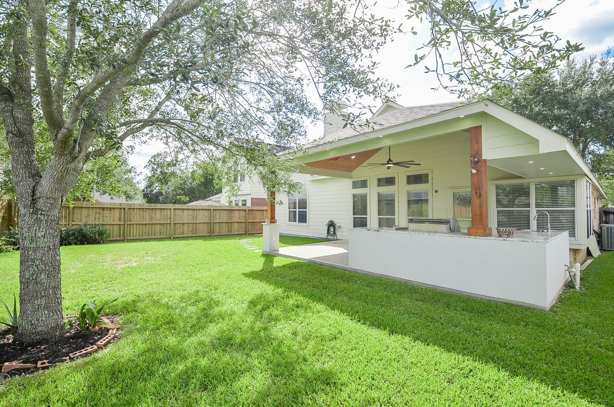 Charming backyard with a spacious covered patio, ceiling fans, and lush green lawn, perfect for outdoor entertaining and relaxation.