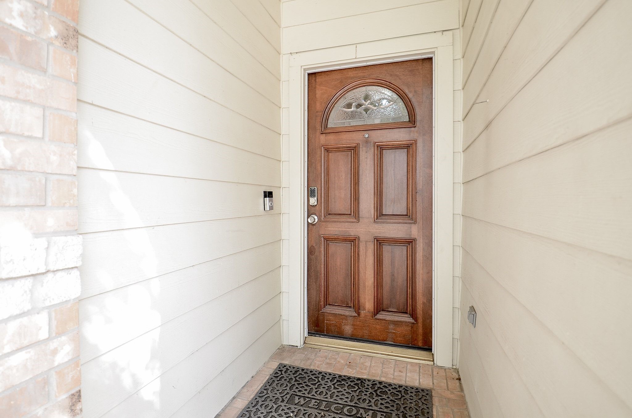 Charming wooden front door with an elegant arched window, set against a welcoming entryway with brick accents.