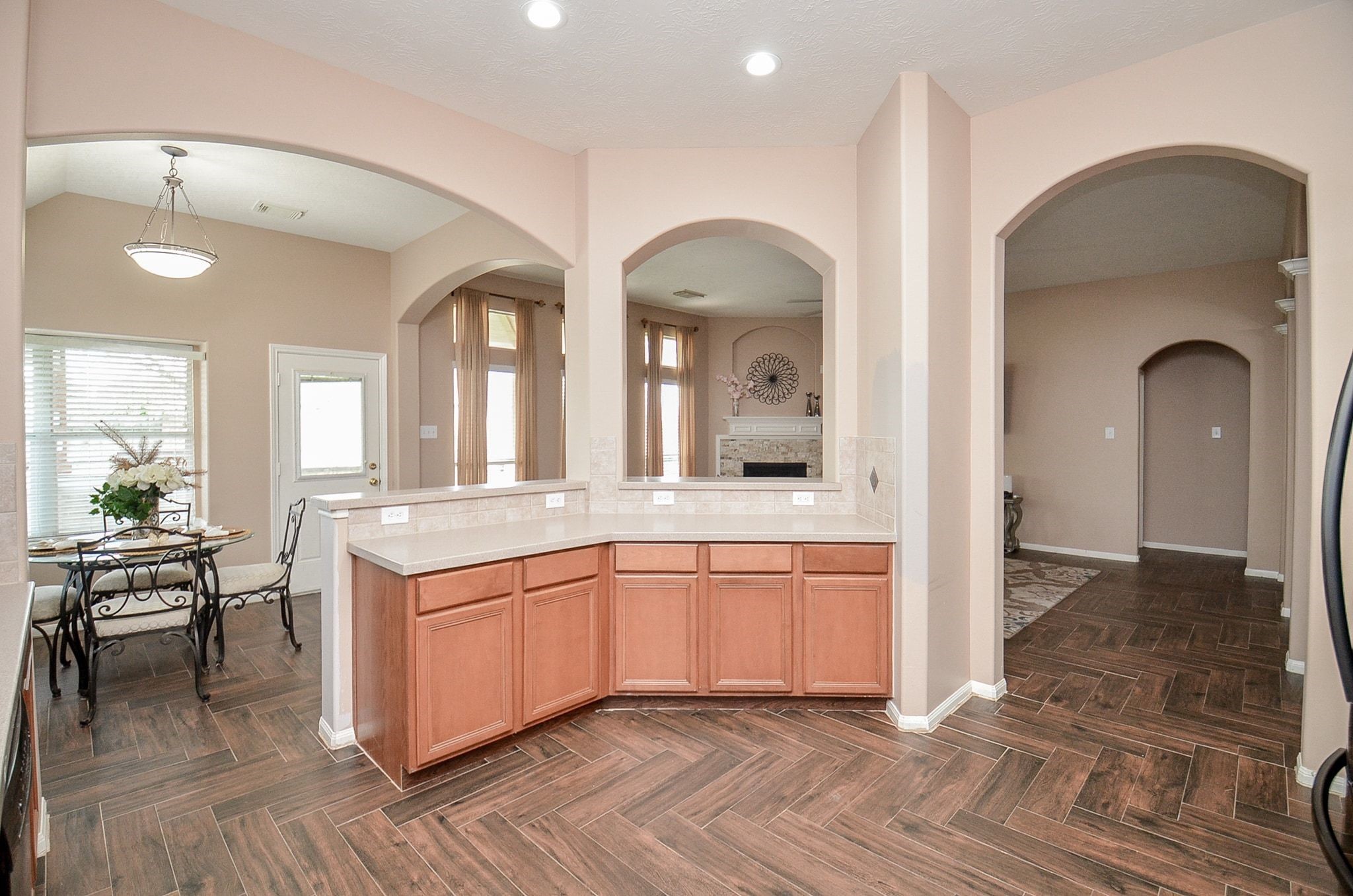 Spacious kitchen with elegant archways, featuring warm wood cabinetry and a sleek tile floor, seamlessly connecting to a cozy dining area and inviting living room.