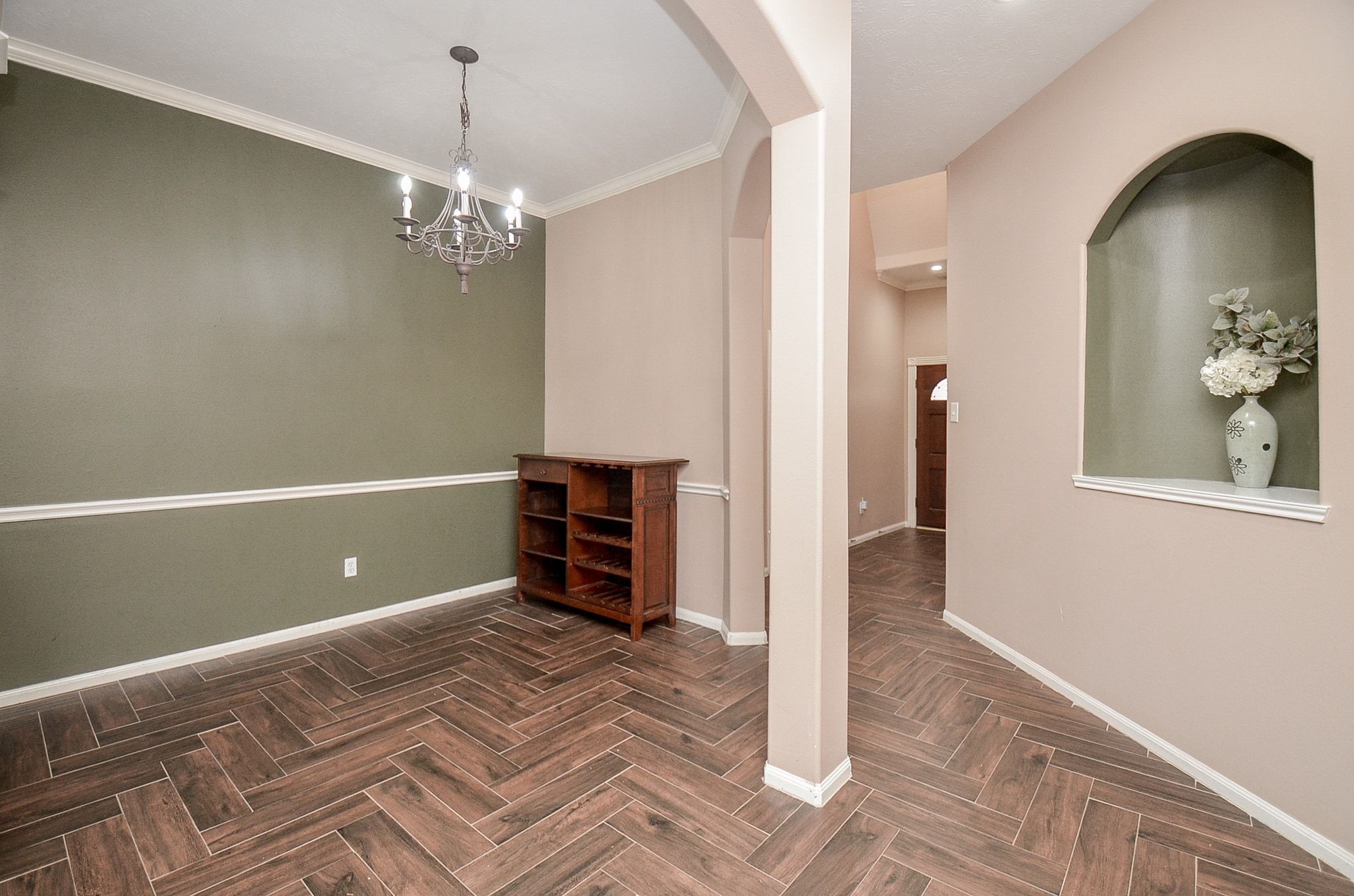 Elegant dining area with herringbone wood flooring, a classic chandelier, and a soothing two-tone wall palette. An arched entryway adds charm and character.