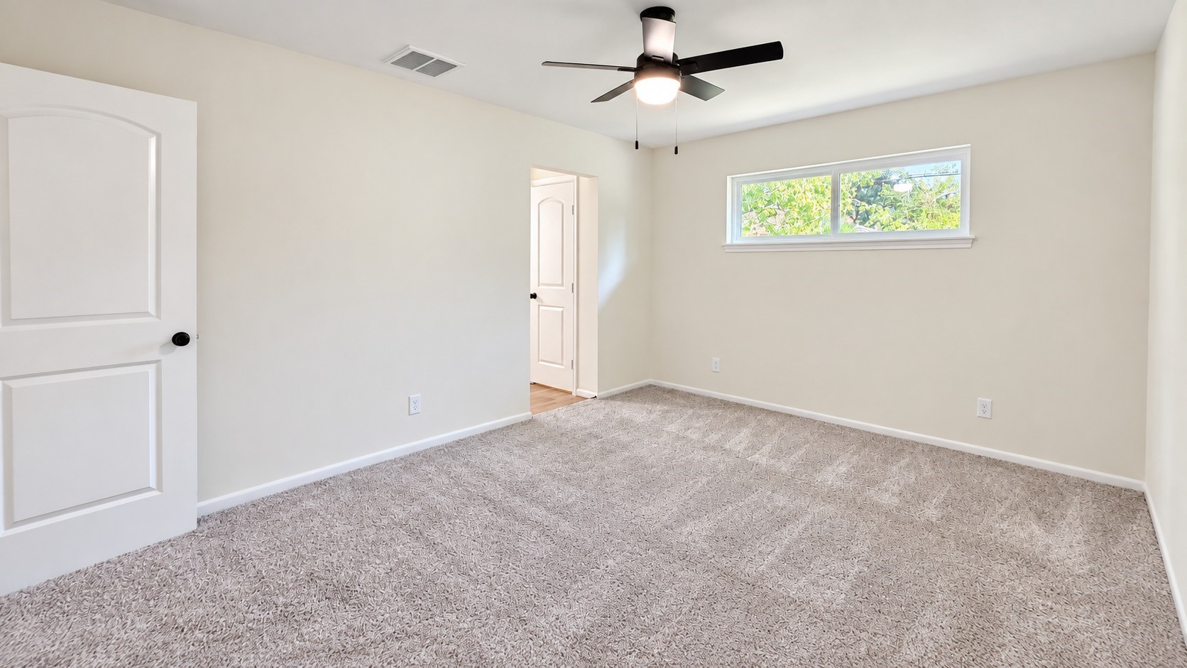 Primary bedroom offers a generous footprint, ceiling fan, soft carpeting, and natural light.