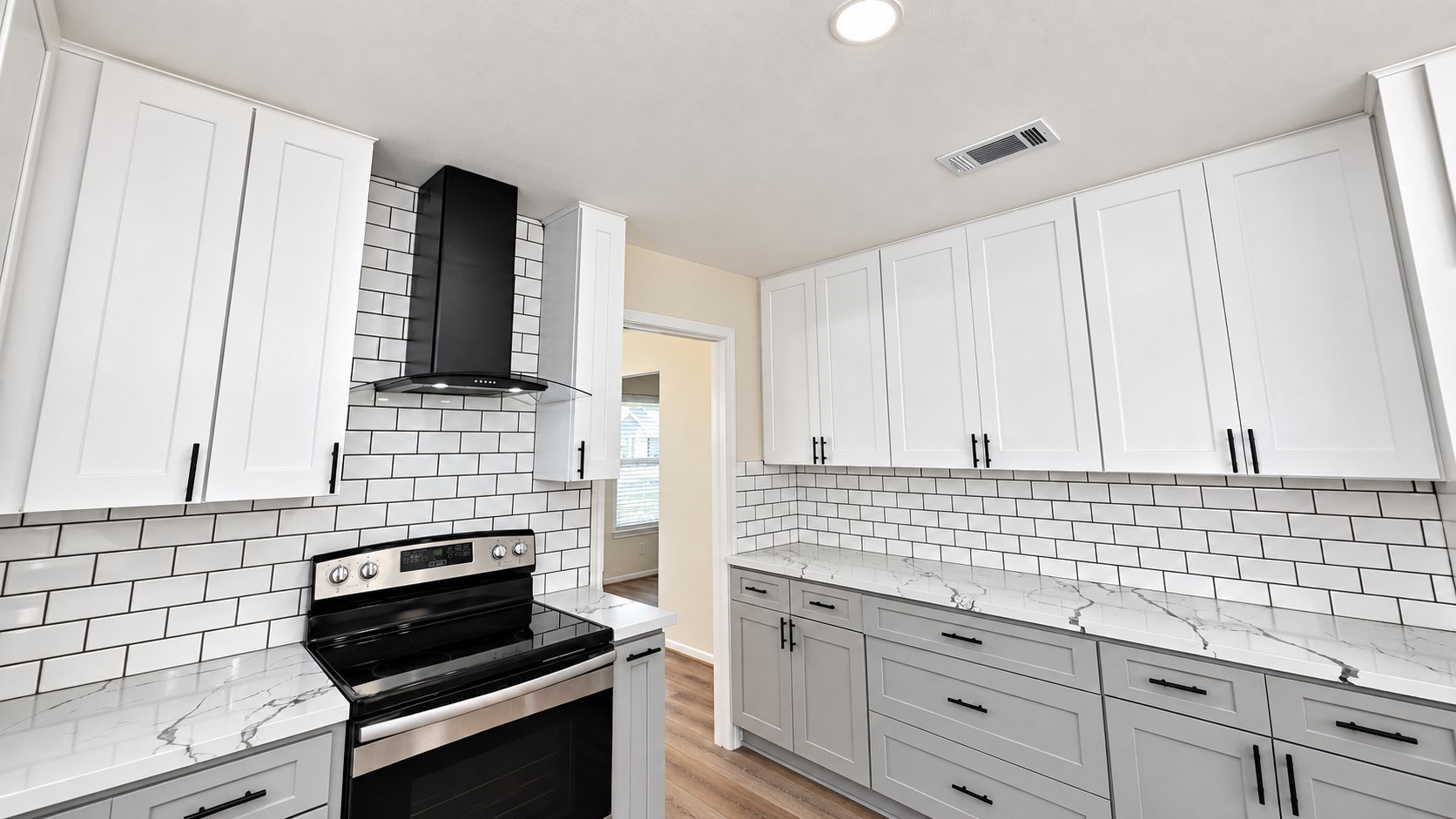 Updated cooking area with stainless range, modern vent hood, subway tile, and generous cabinet storage.