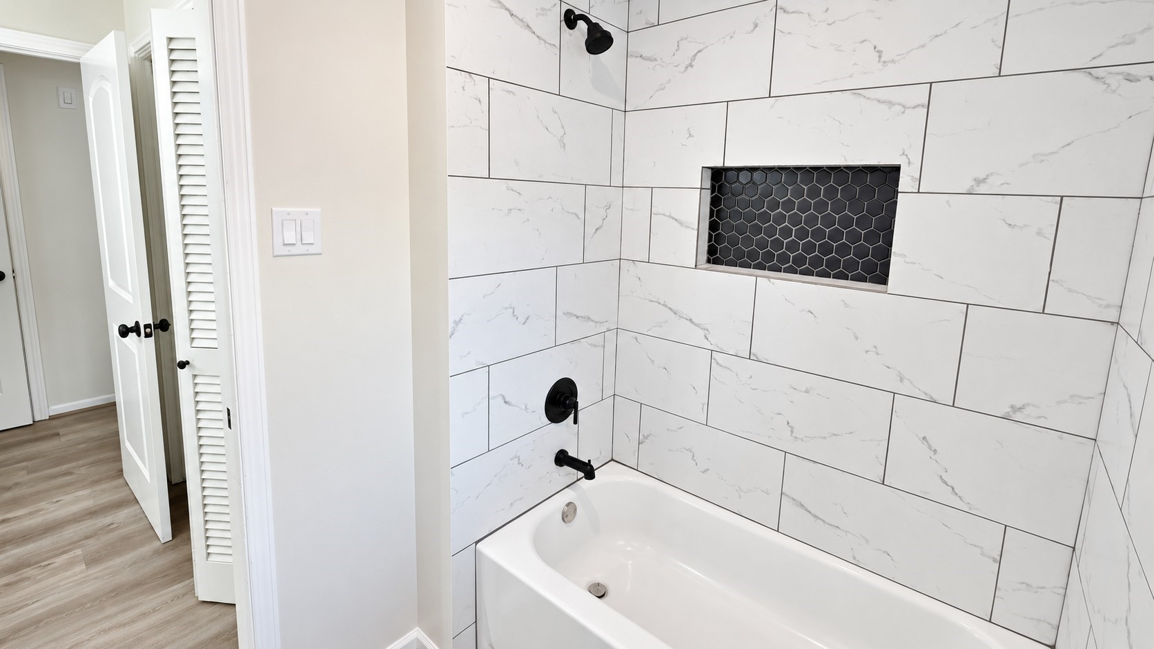 Secondary bath includes a tub/shower combination surrounded by modern large-format tile and a built-in niche.