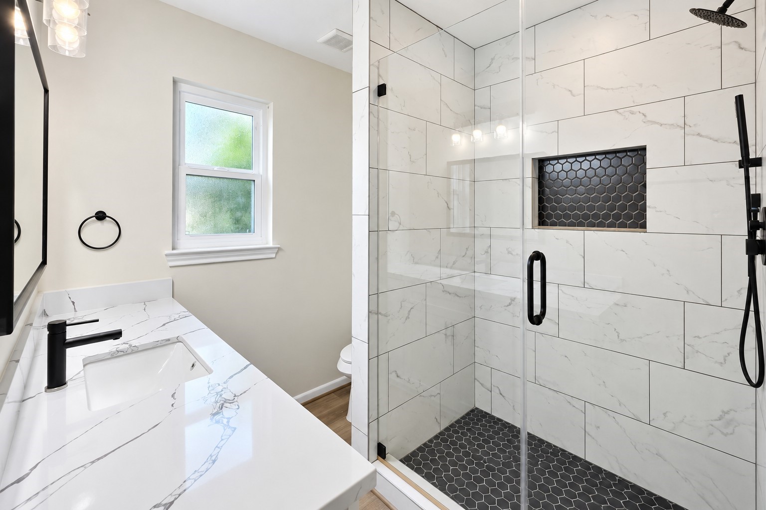 Primary bath features a striking glass-enclosed walk-in shower with oversized tile, niche, and matte-black fixtures.