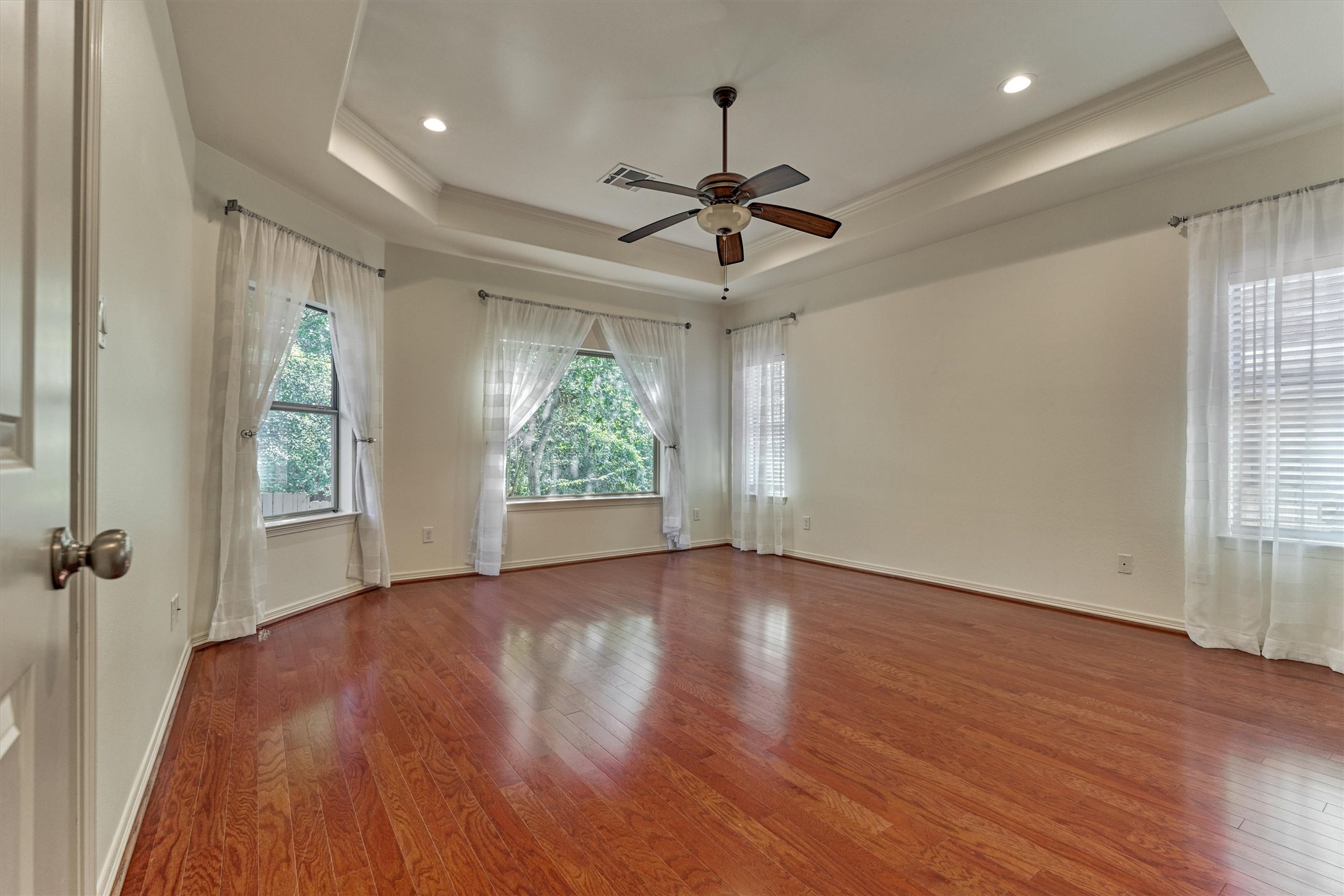 The large primary bedroom features a tray ceiling and plenty of natural light. Large windows overlook the private and serene backyard.