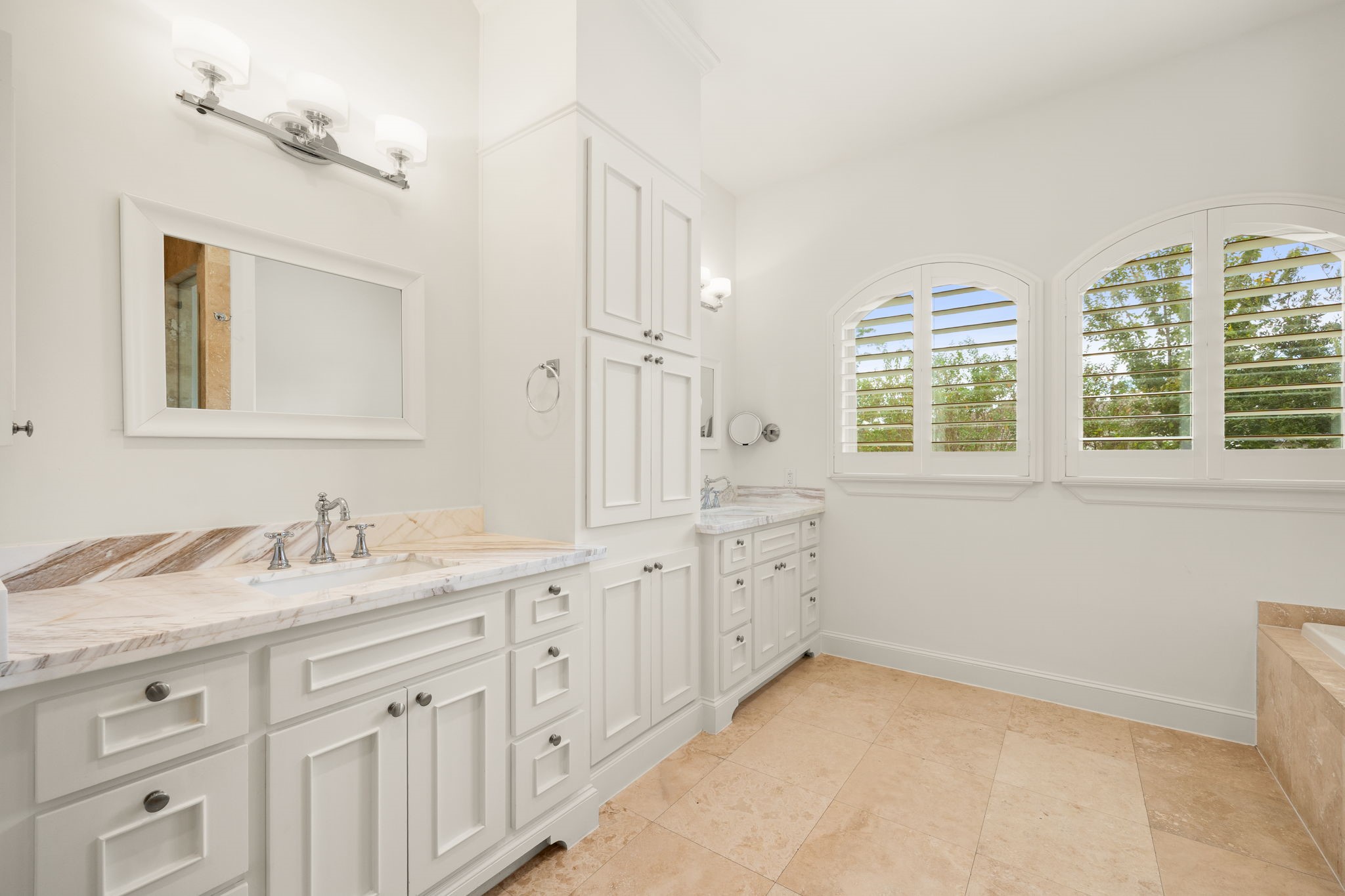 Step into a beautifully appointed primary bathroom, where elegant white cabinetry, marble countertops, and polished chrome fixtures create a timeless, spa inspired atmosphere. Arched windows fill the space with natural light, while the expansive dual vanity offers plenty of room to get ready and enjoy a peaceful start to your day!