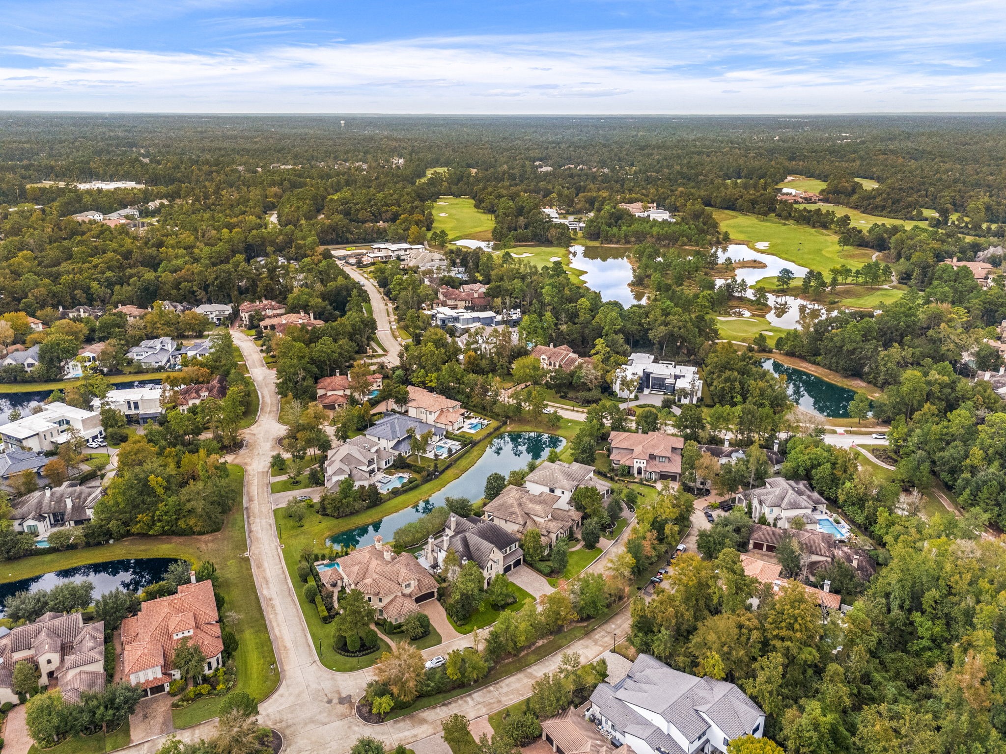 A stunning aerial view showcasing the beautiful lake, surrounded by luxury homes, lush greenery, and the picturesque golf course of Carlton Woods Creekside.