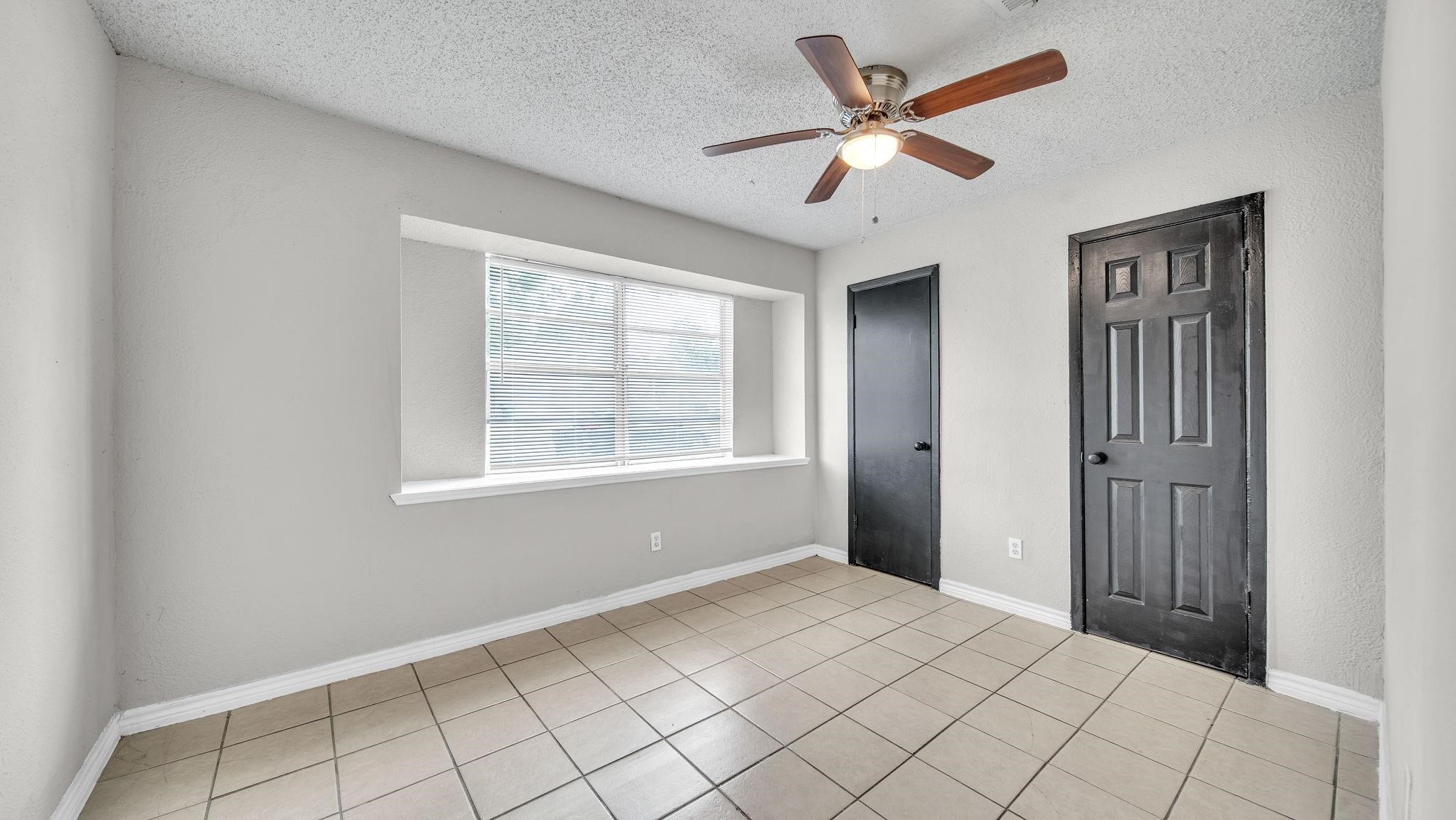 The primary suite offers a serene retreat, featuring elegant tile flooring, a ceiling fan with integrated lighting and a spacious walk-in closet with ample storage for an organized wardrobe.
