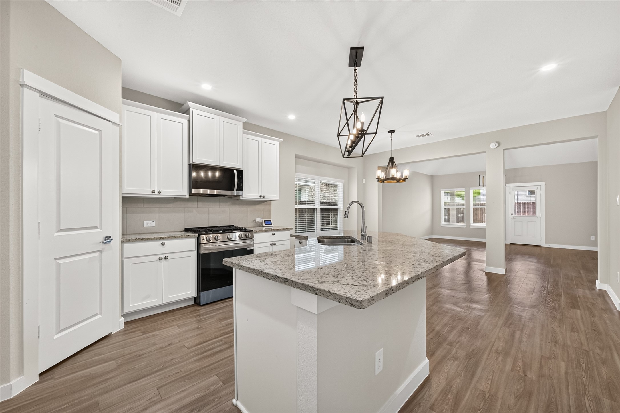 White cabinetry, granite countertops, stainless steel appliances, and upgraded lighting complement this bright kitchen.